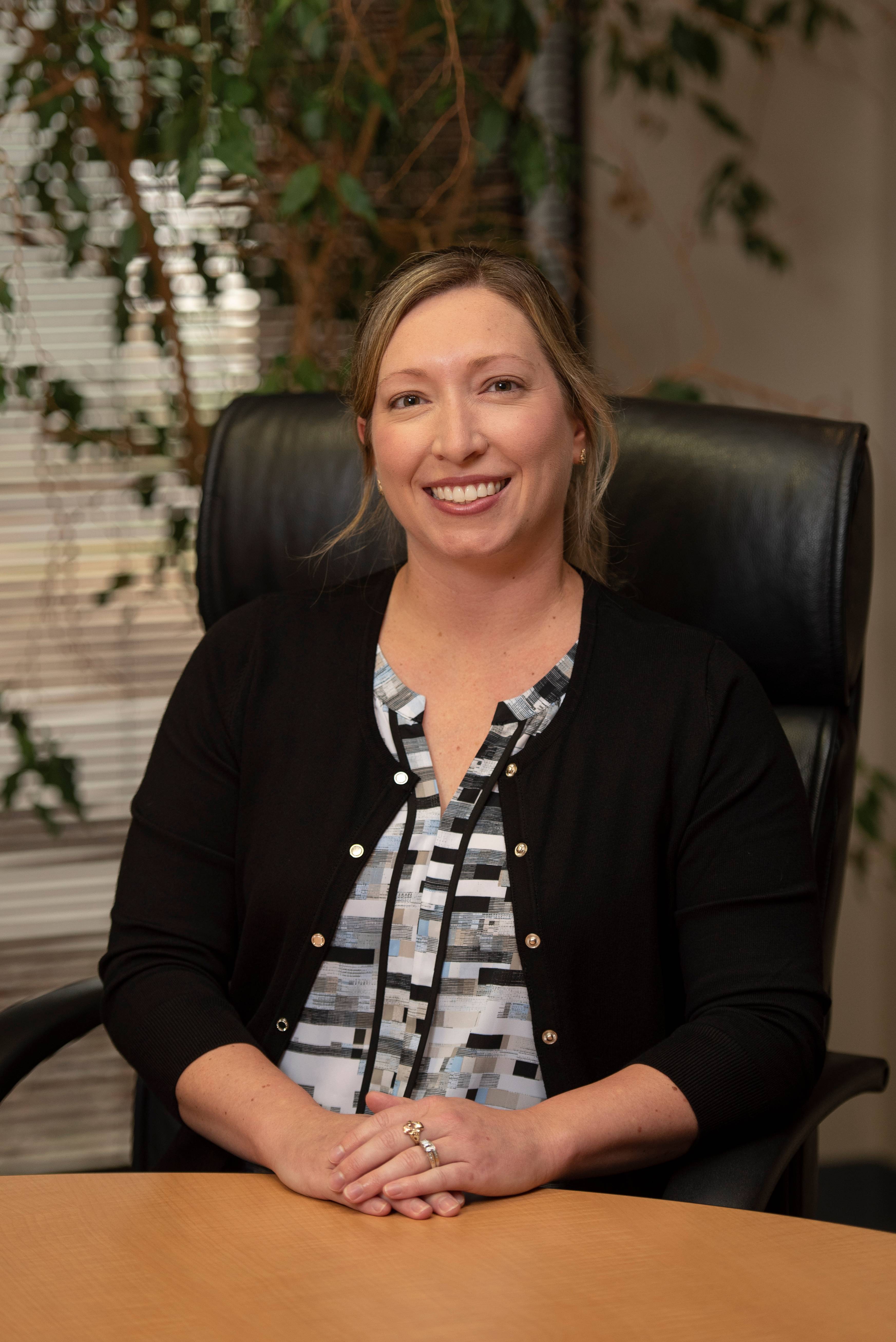 woman wearing a black blazer sitting behind a desk and smiling at camera