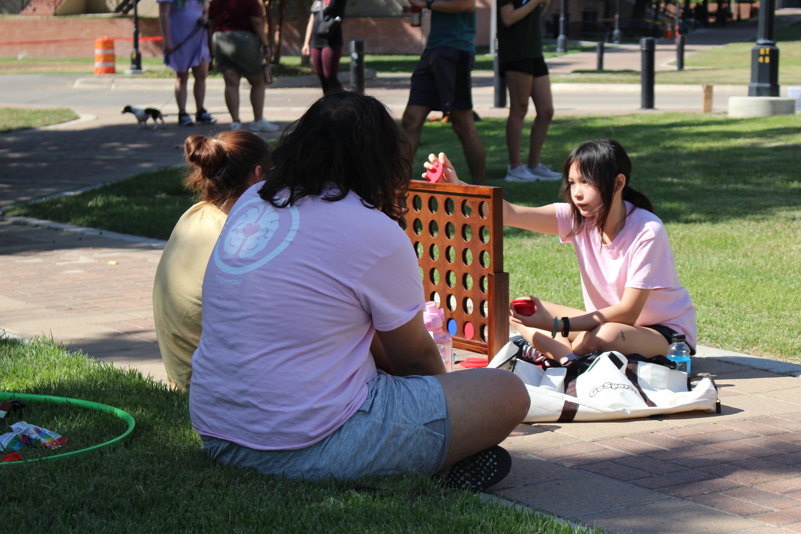 Three people in pink shirts playing connect four outside