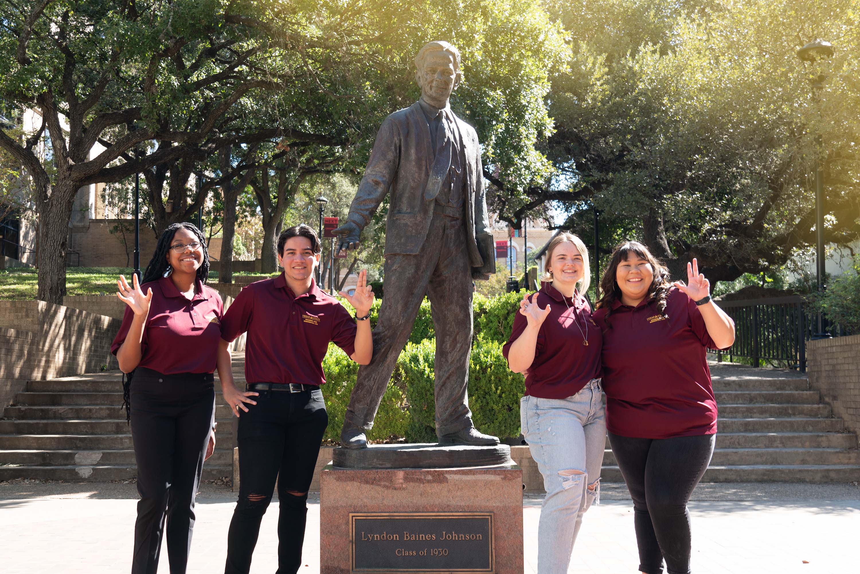 Four students in maroon polos next to LBJ statue