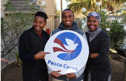Mohamed Hassan-Issa stands holding a Peace Corp sign with family members on either side of him