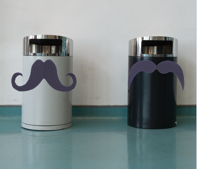 An image of two trash cans in a hallway with large cardboard mustaches.