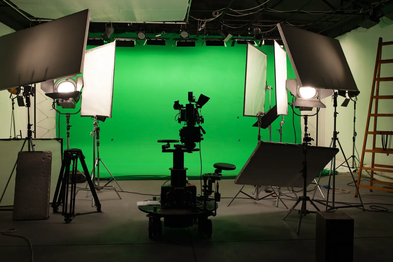 Video production studio full of lights, camera rigs, and shaders. On the back wall is a green screen backdrop