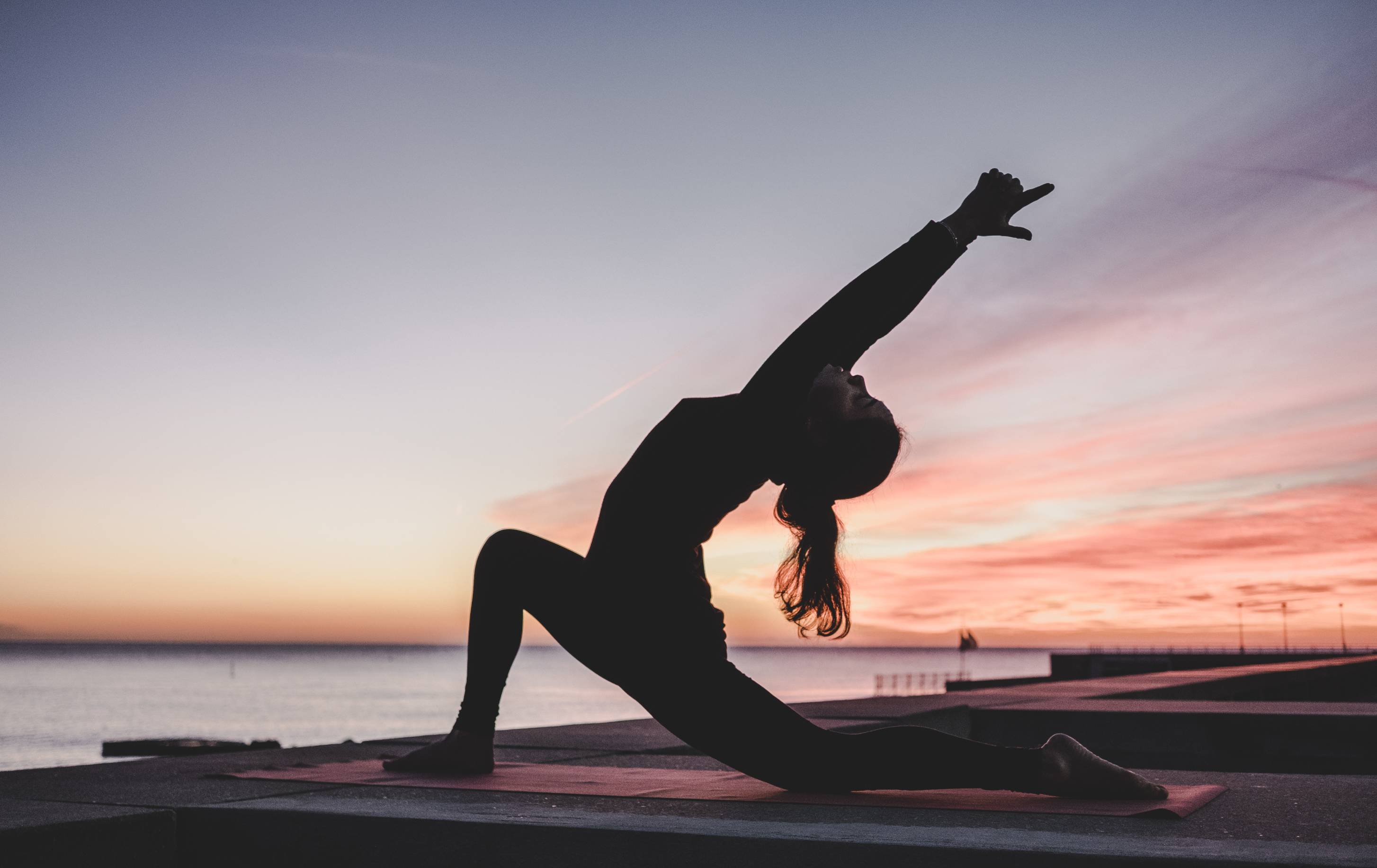 Image of the silhouette of a person doing yoga. A sunrise is in the background.
