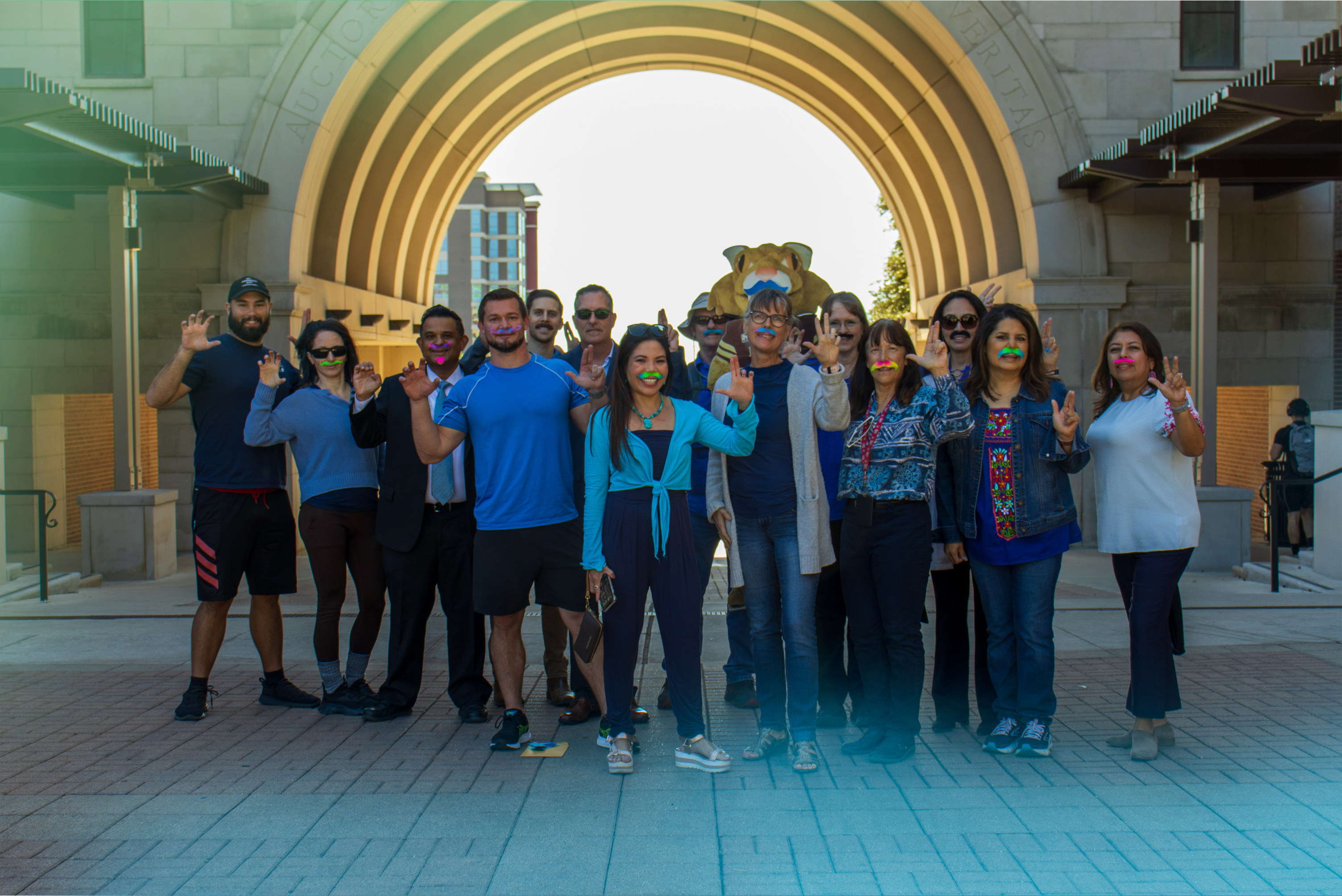 A group of TXST employees wearing blue and fake mustaches at the THH Arch.