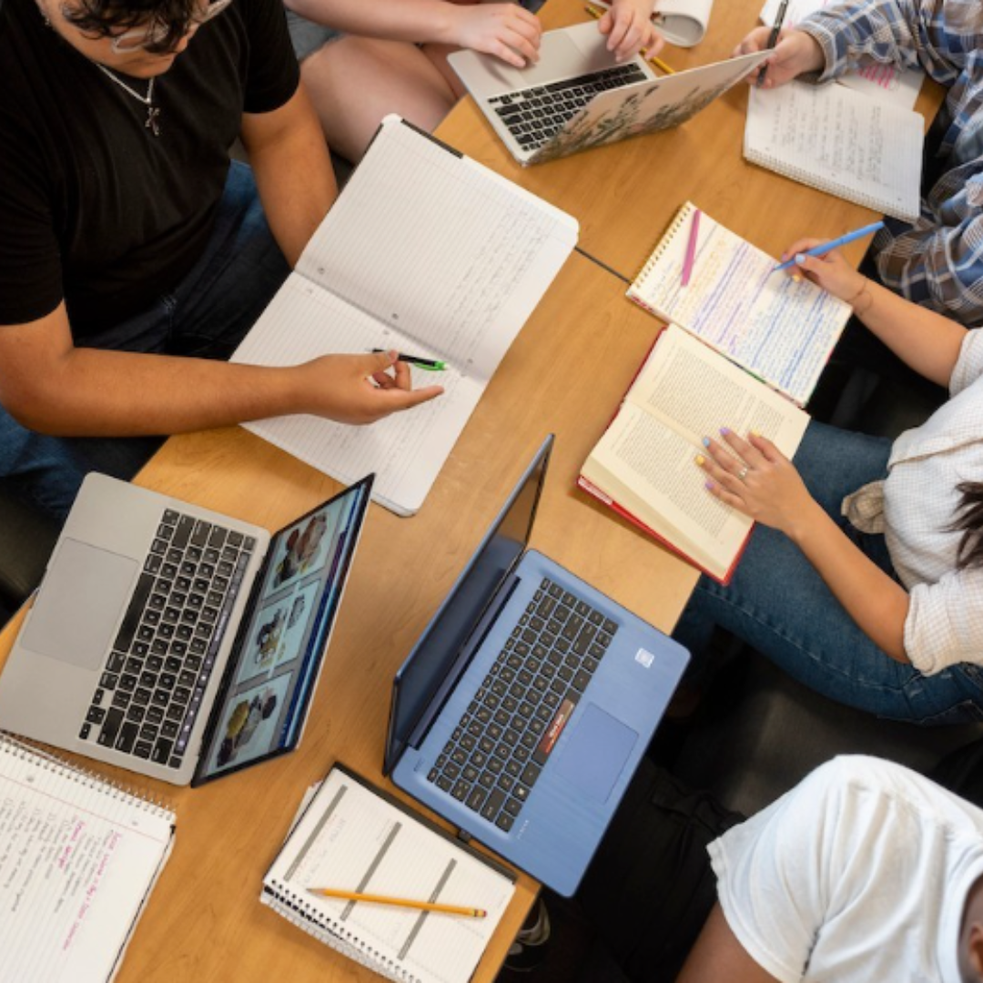 students gathered around studying with notebooks and laptops on tables