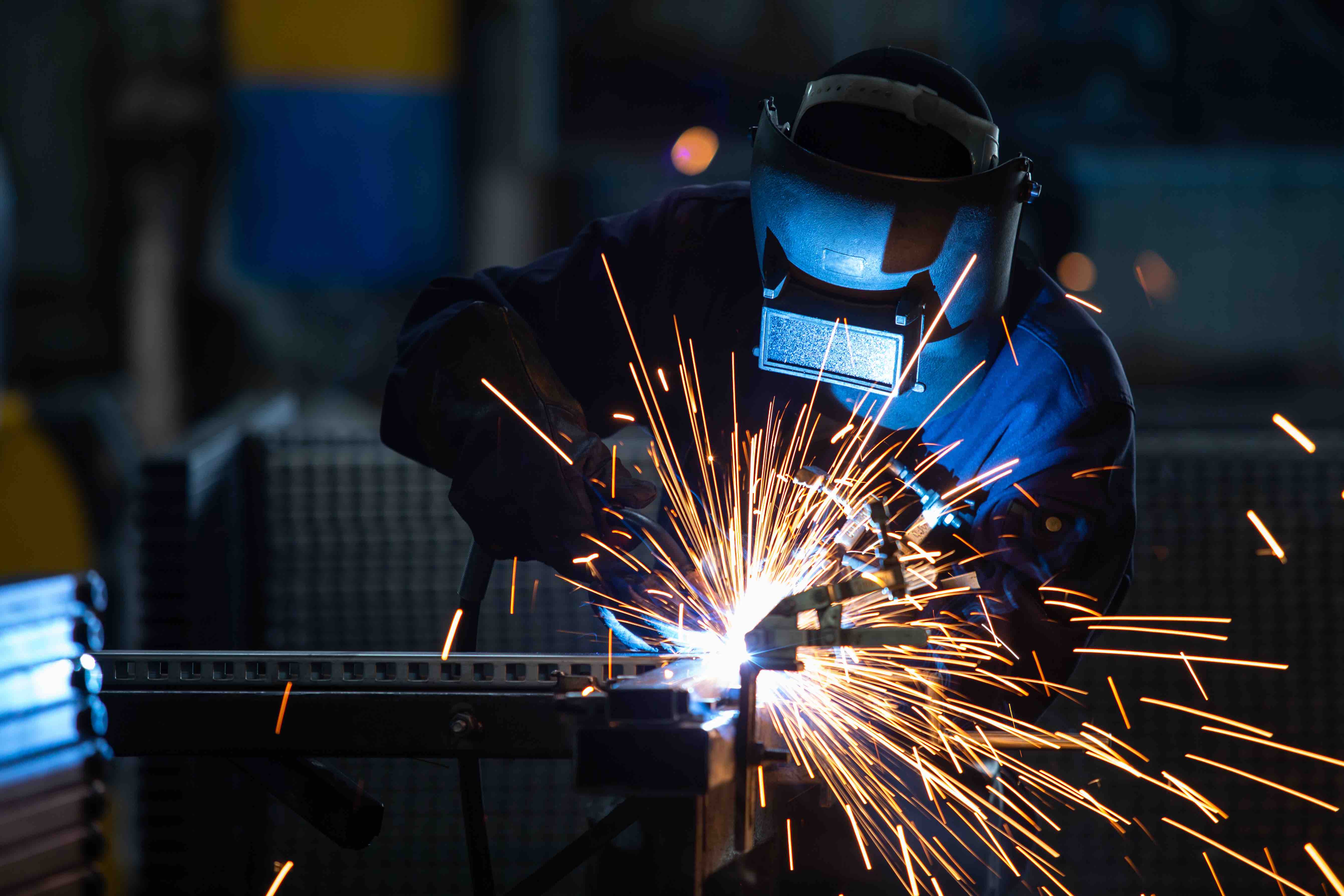 A person welding wearing a welding mask with flying sparks.