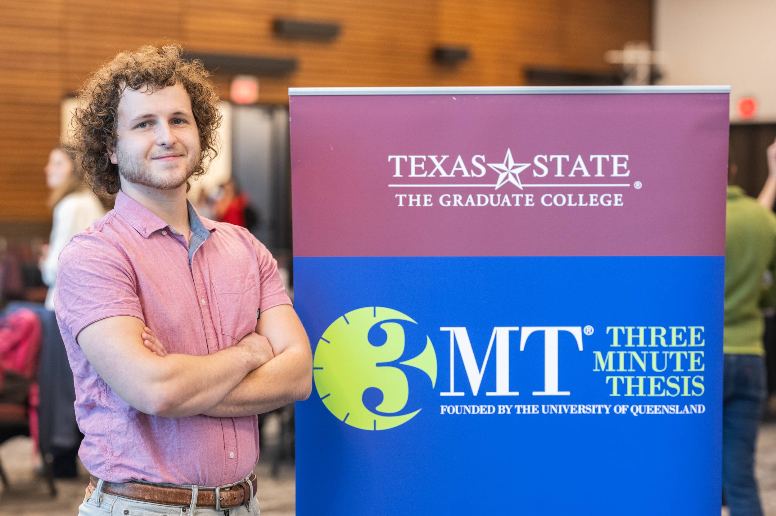 Joshua Rogalski standing next to a 3MT sign with her arms crossed