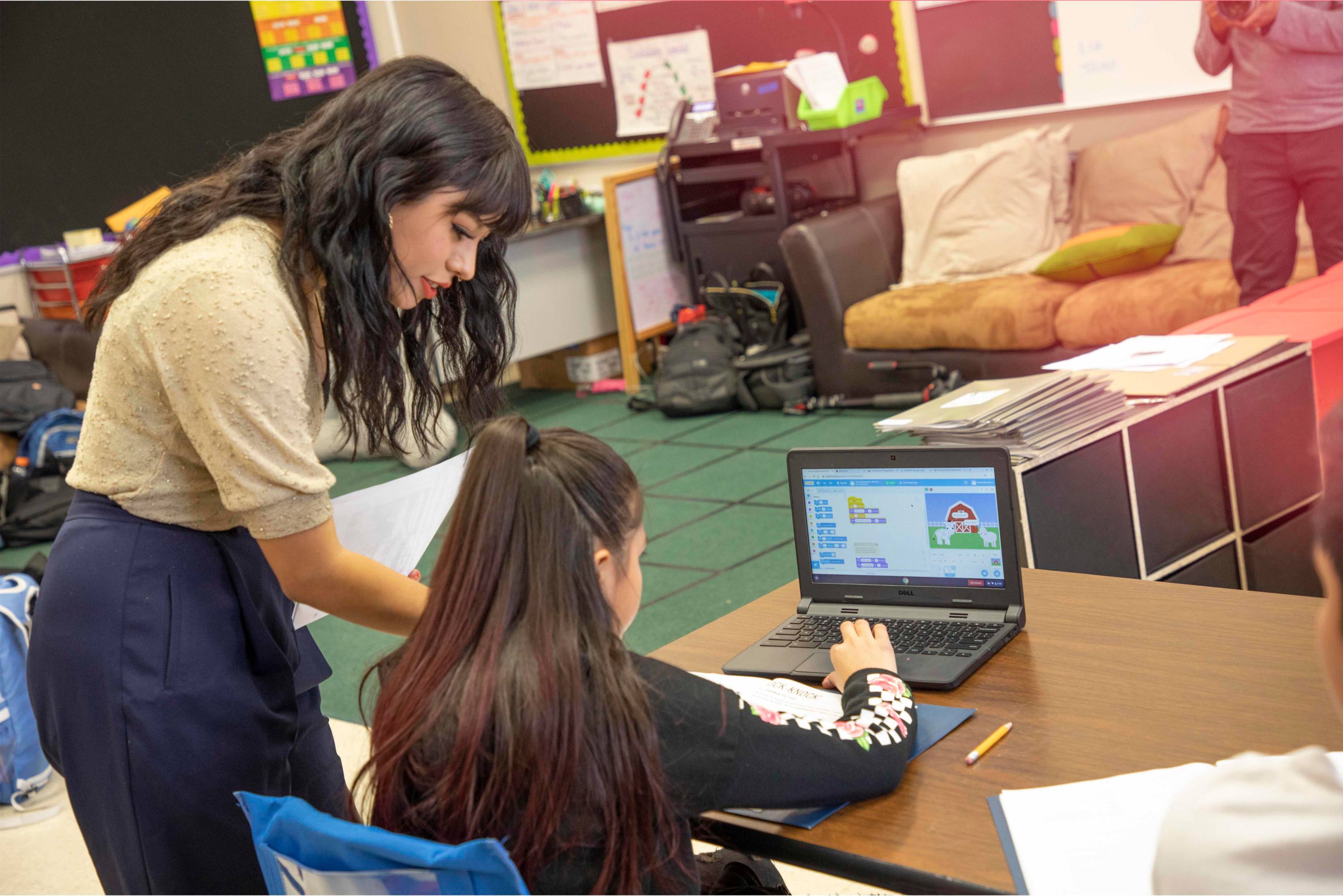 A teacher showing a child how to use a computer program in a classroom.