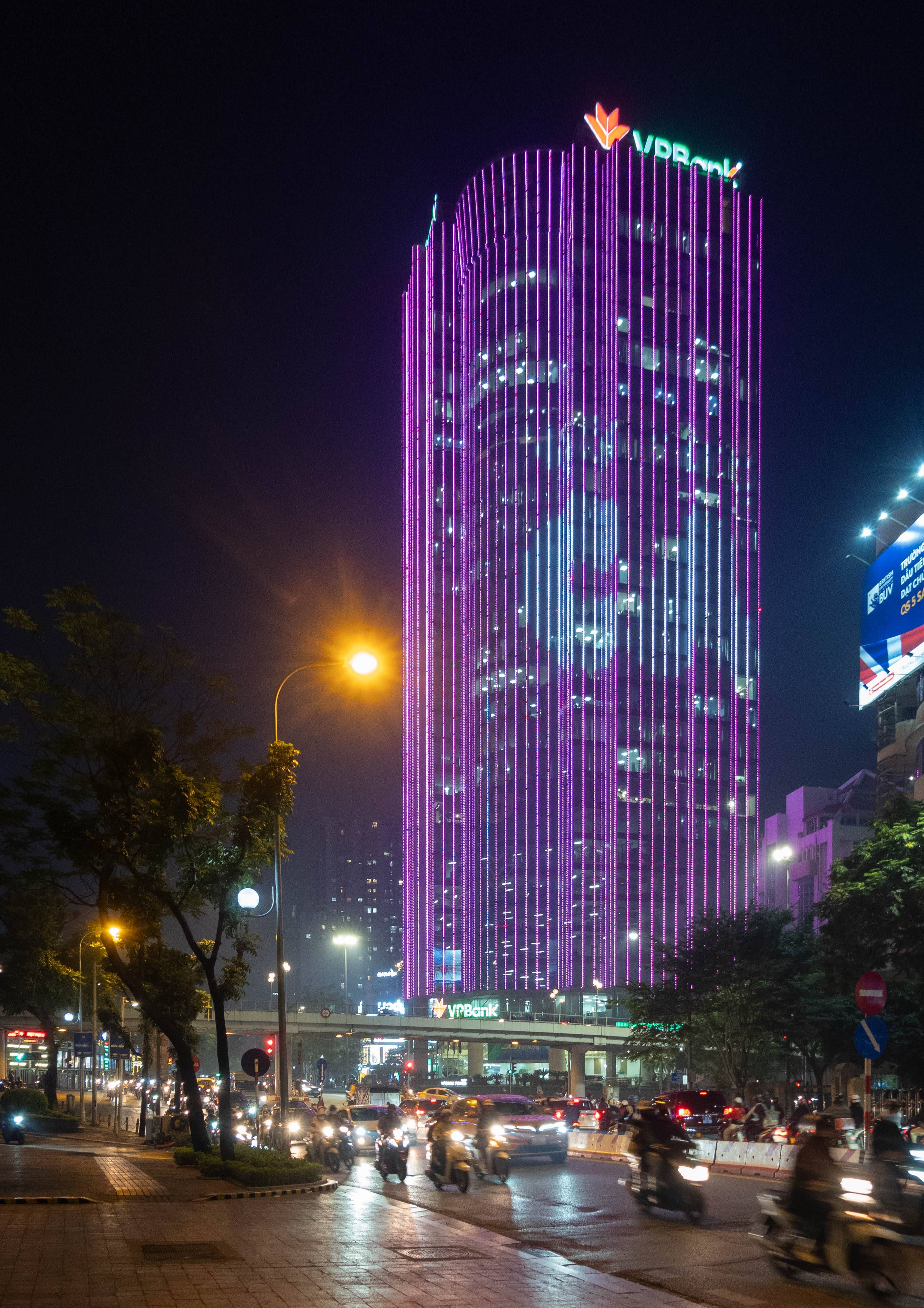 picture of tall building with purple neon with traffic on street below 