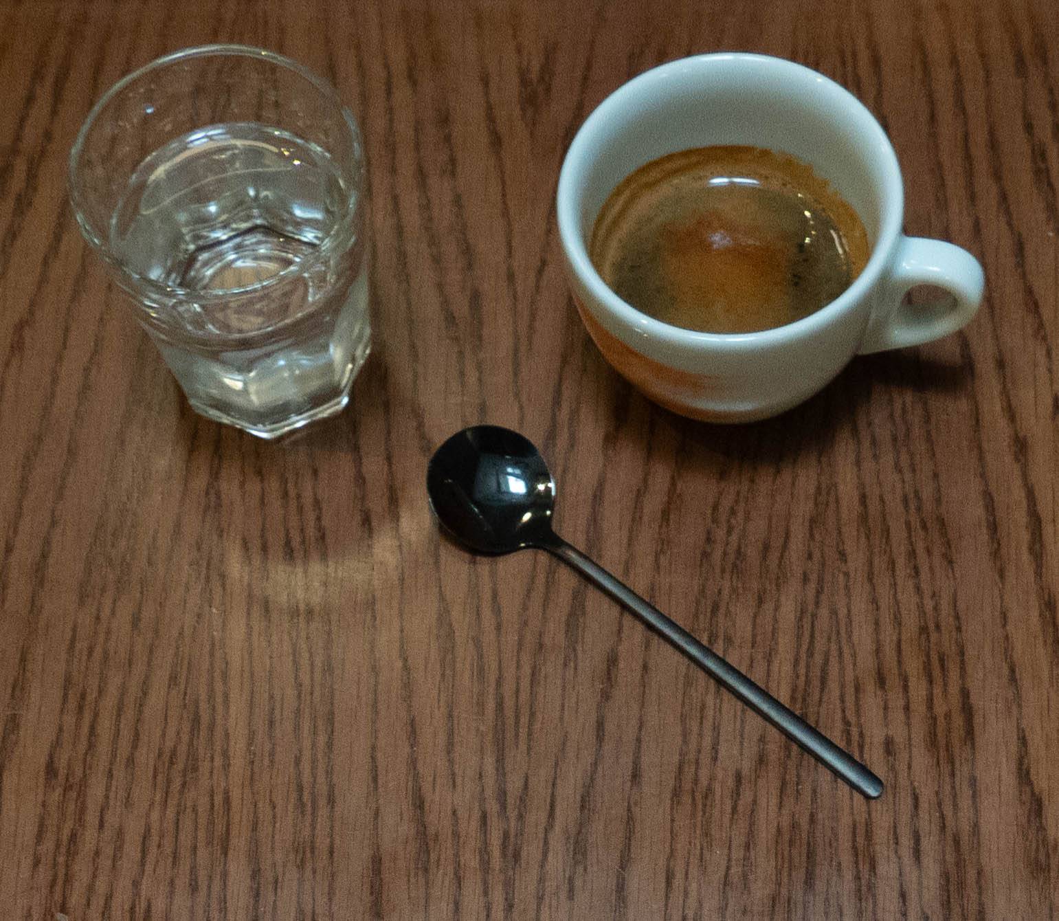 picture of cup of black hot coffee on right and shot glass of water on left
