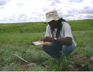 student kneeling in a field reading a book