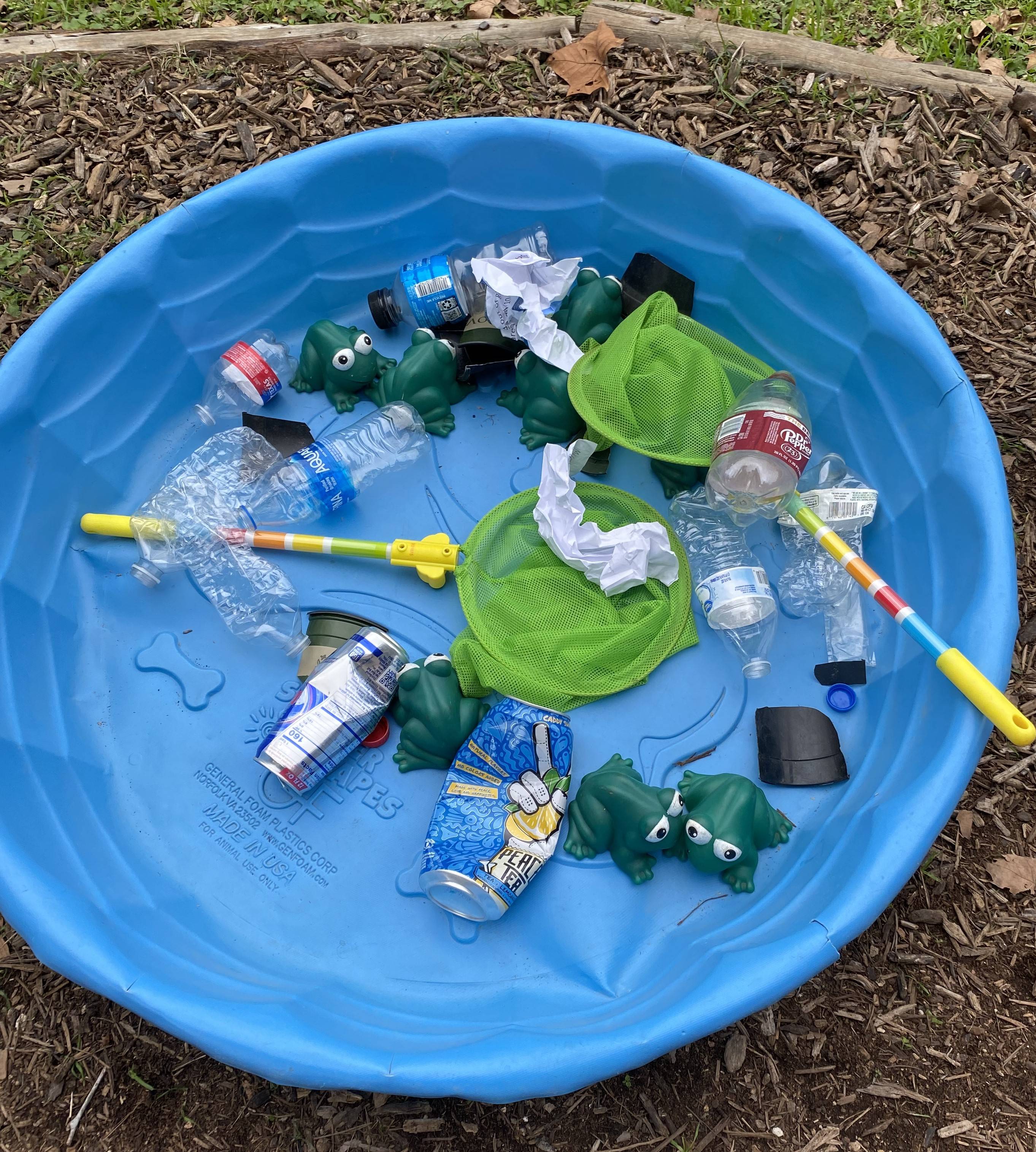 Plastic frogs are surrounded by litter in a blue kiddie pool from which students must fish out pollutants to symbolize keeping our natural environment clean.