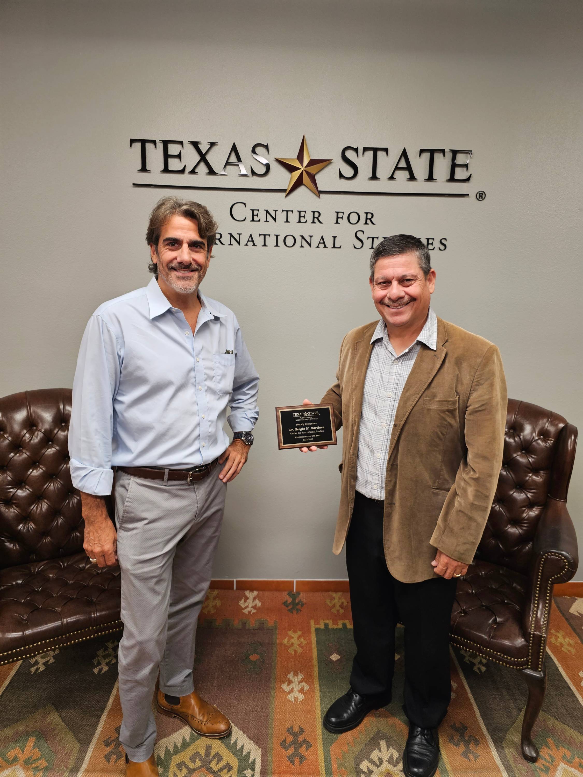 Dr. Paul Hart and Dr. Sergio Martinez stand in front of the IS logo with an award plaque