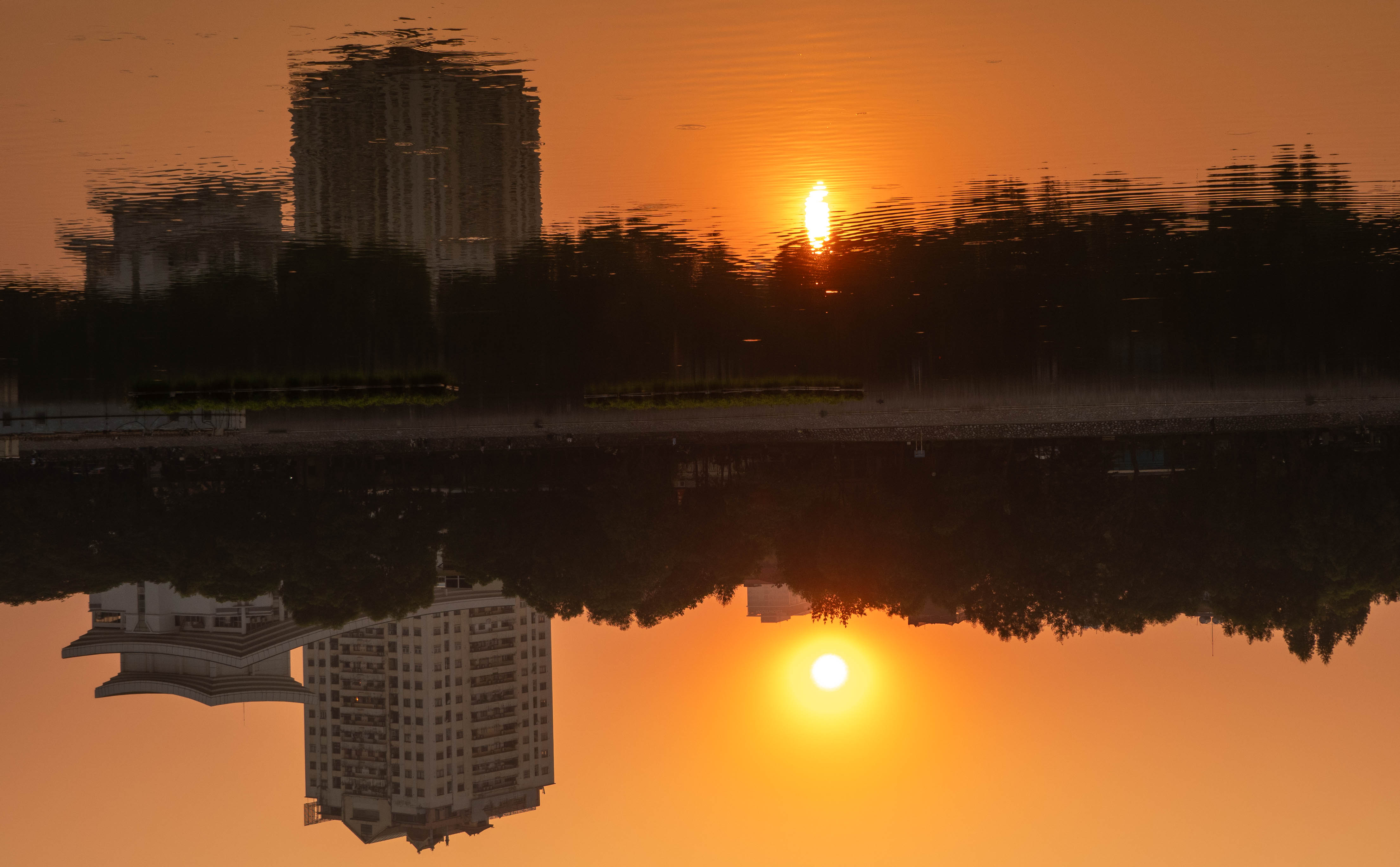 Inverted picture. This is a picture of two buildings by the lake at sunset. The sun is in the sky and the reflection of the sun looks like it is the fire of a candle