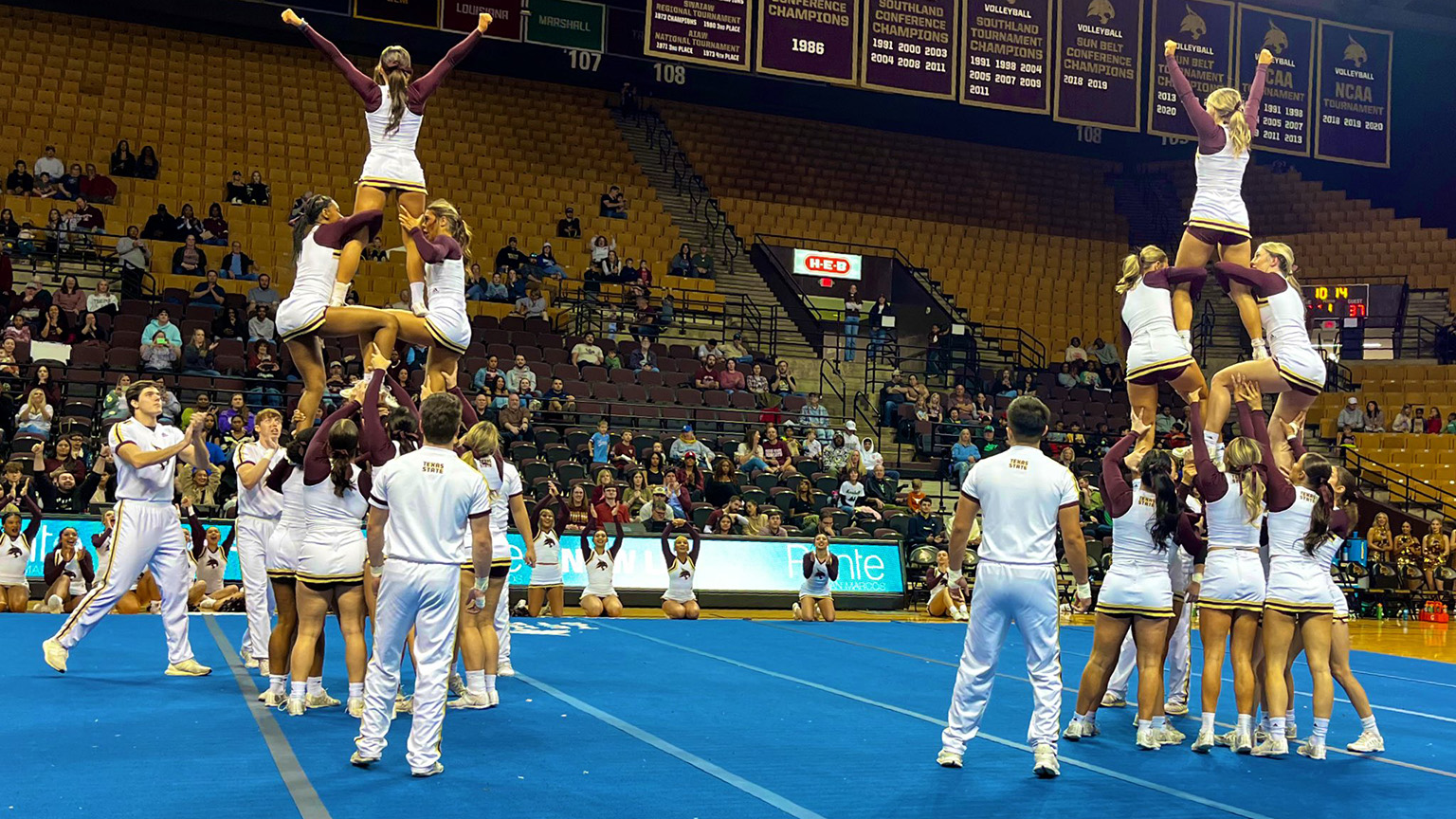 Several TXST Cheer members practice their competition routines in front of a small crowd.