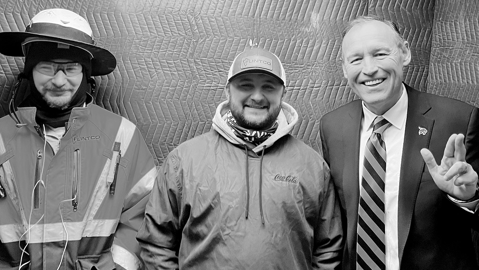 Two construction workers pose for a photo with President Damphousse, right.