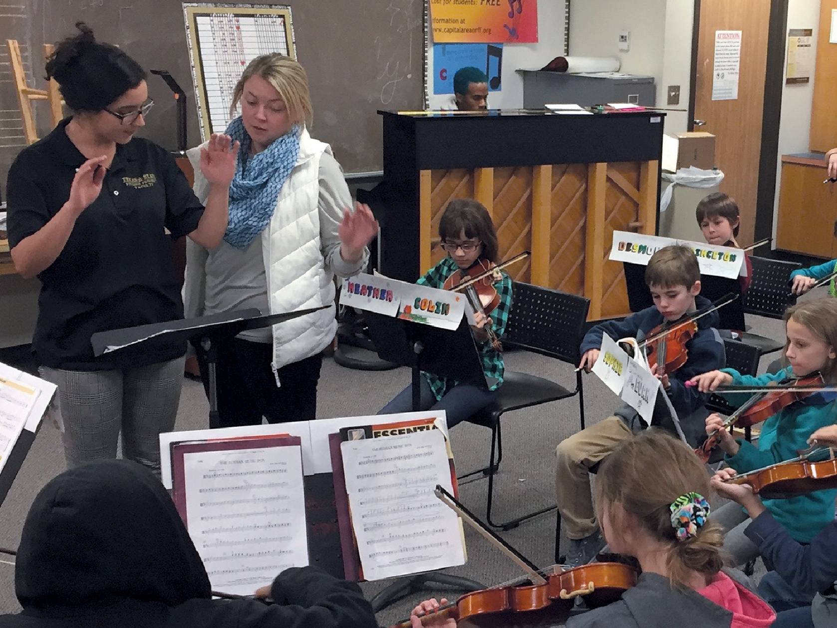 A female string teacher assists a student conductor in directing a youth string ensemble.