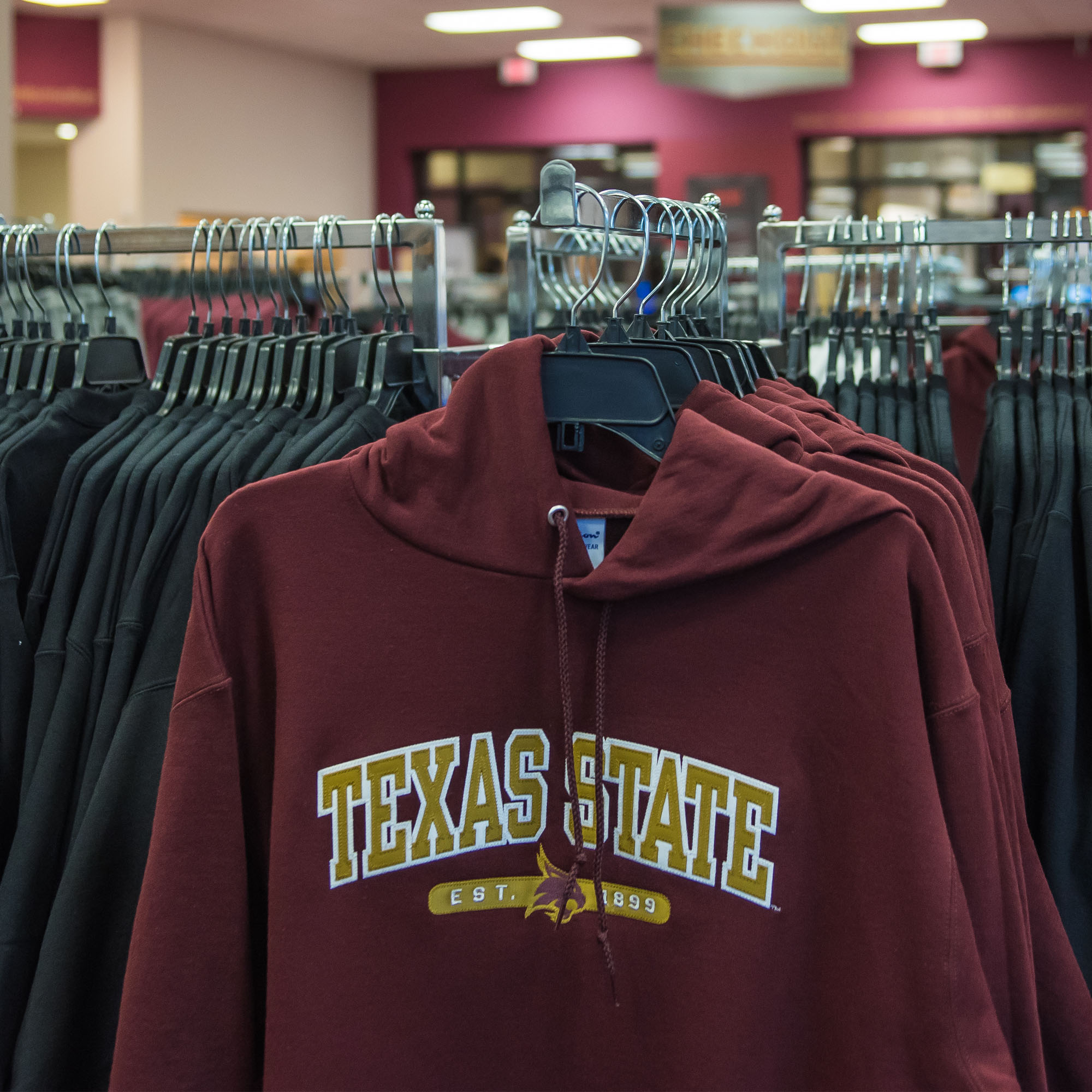 Texas State hoodie on a rack, in front of other hoodies, in University Bookstore.