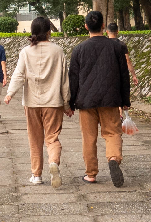 Woman (right) and man (left) walking hand in hand . Man on right has a clear plastic bag with koi in it.