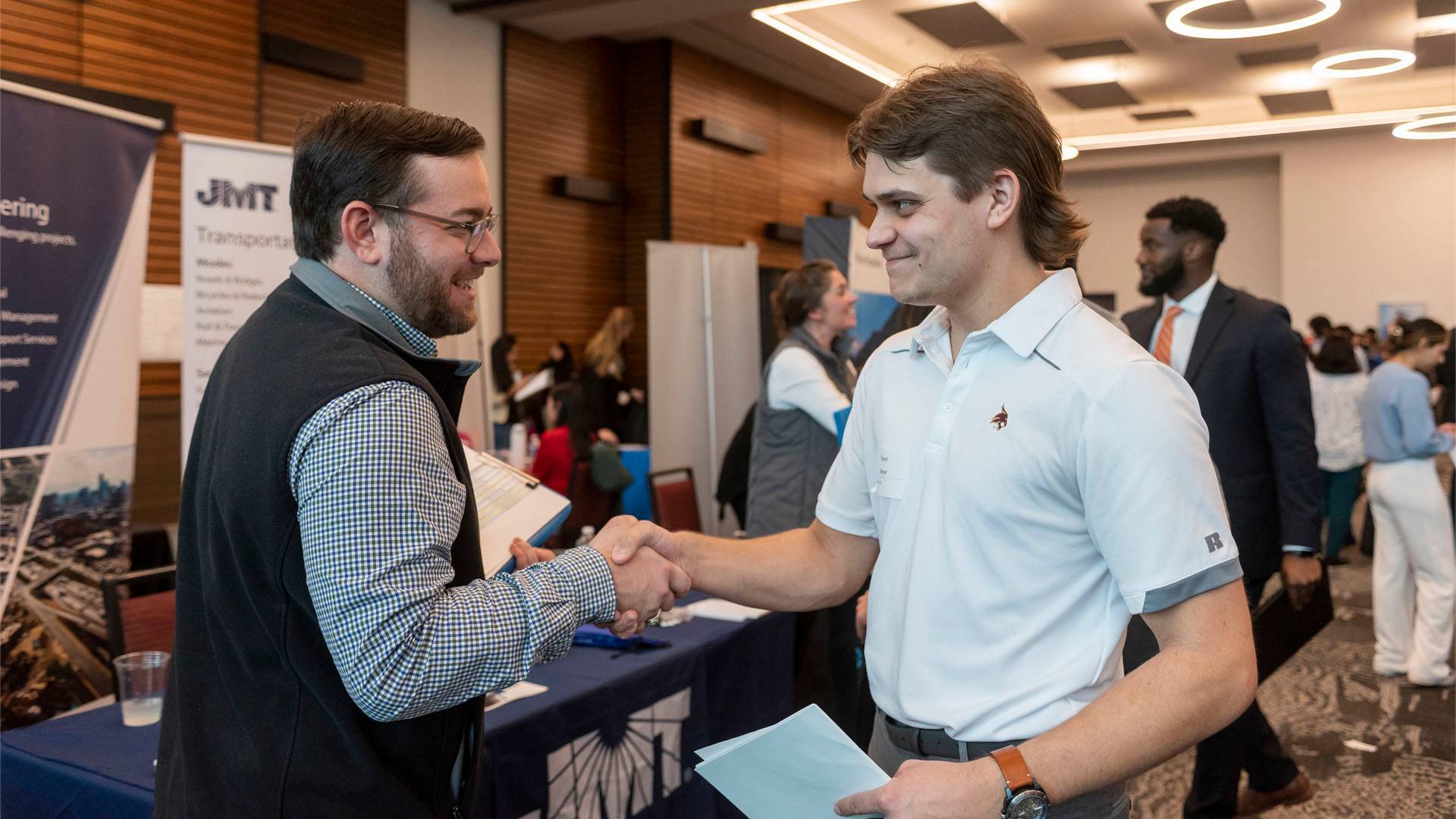 Two men shaking hands and smiling at a career fair.