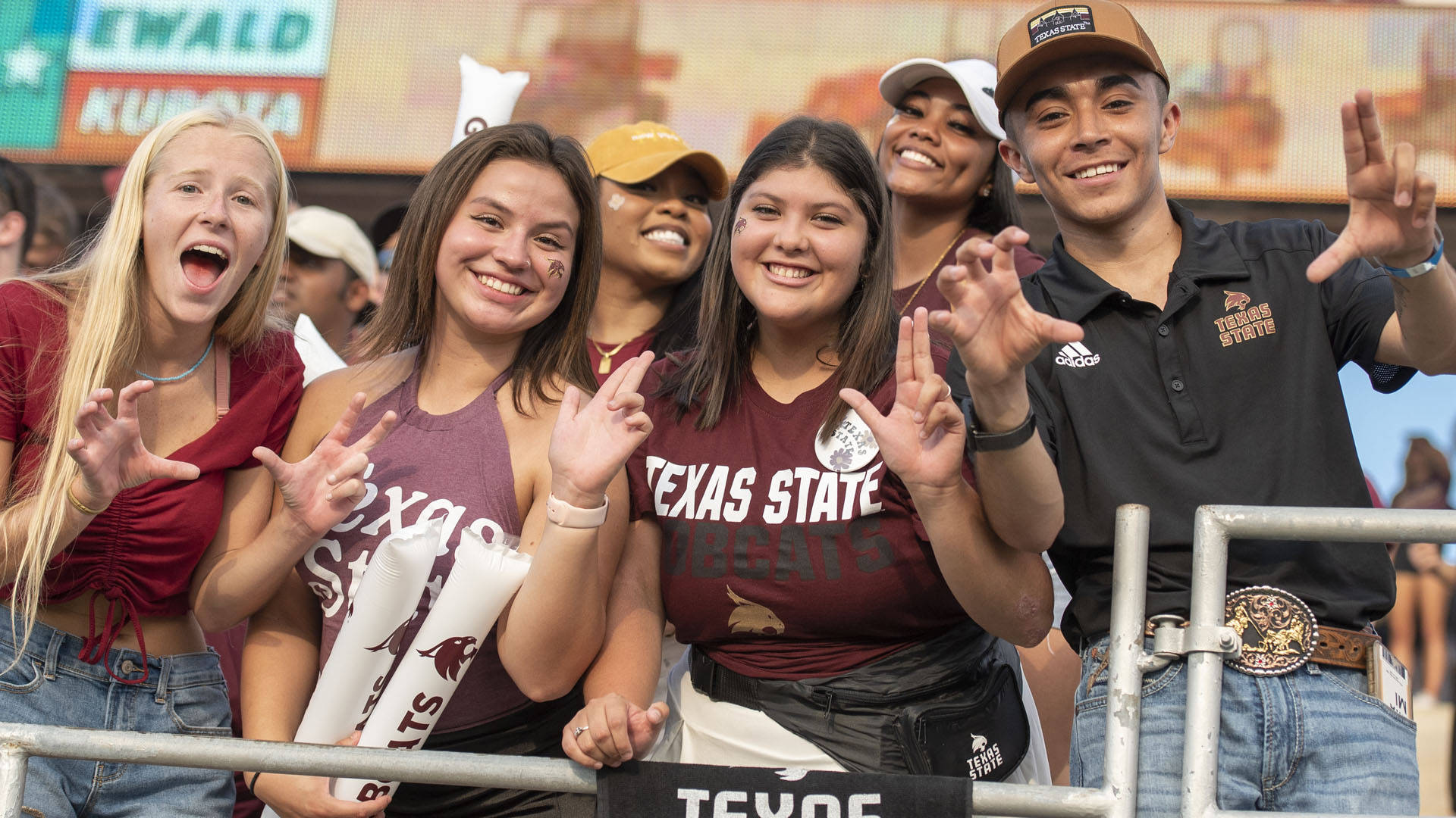 group of students smiling and making Texas State hand symbols at a Texas State Football game