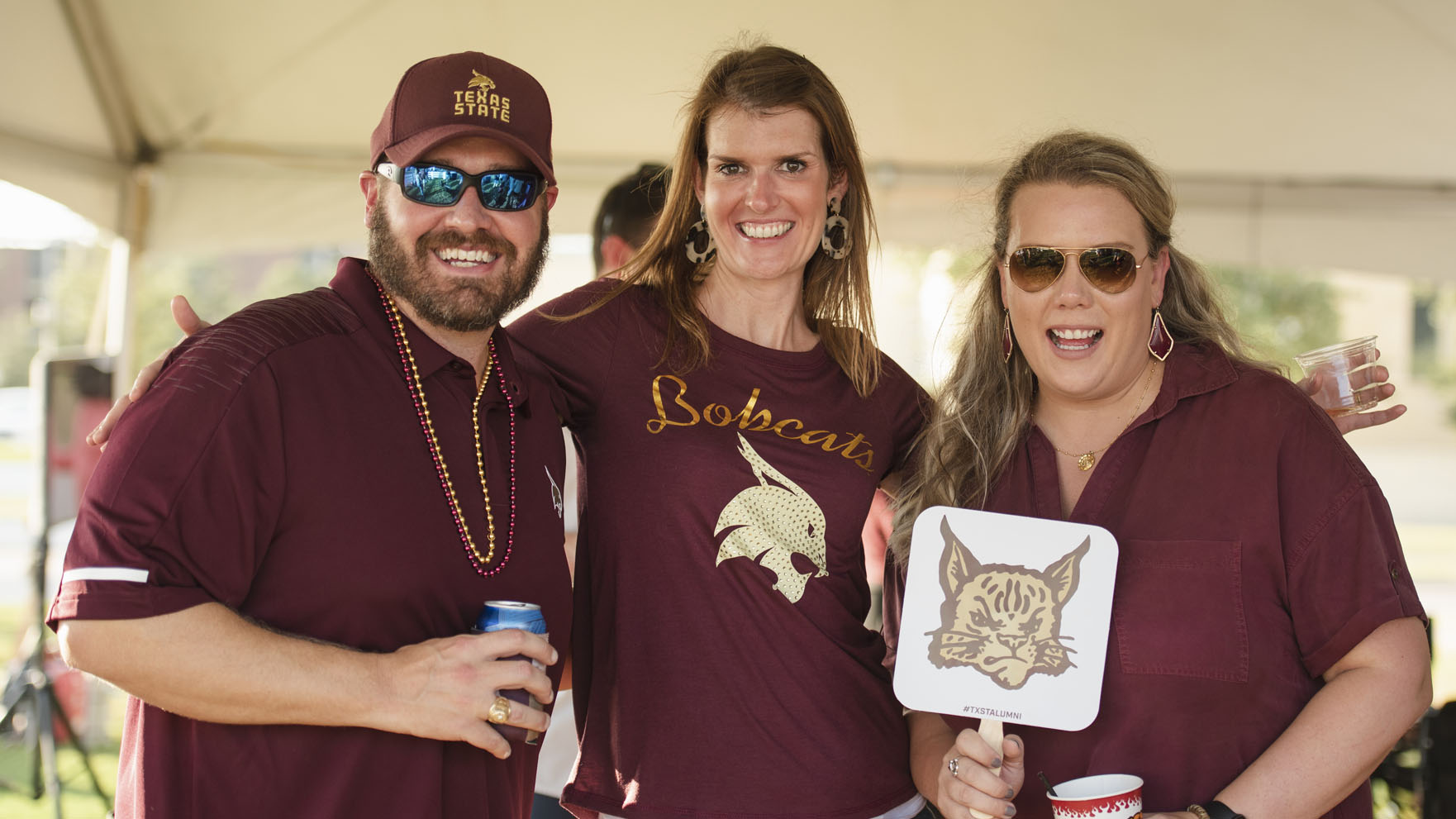 photo of three people, wearing Texas State gear, at a tailgate
