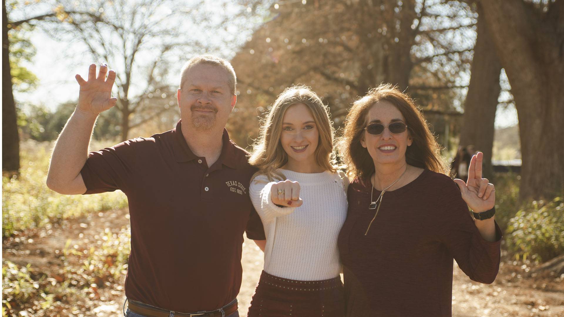 photo of Texas State student next to their parents, trying on Texas State Ring, showing it to the camera