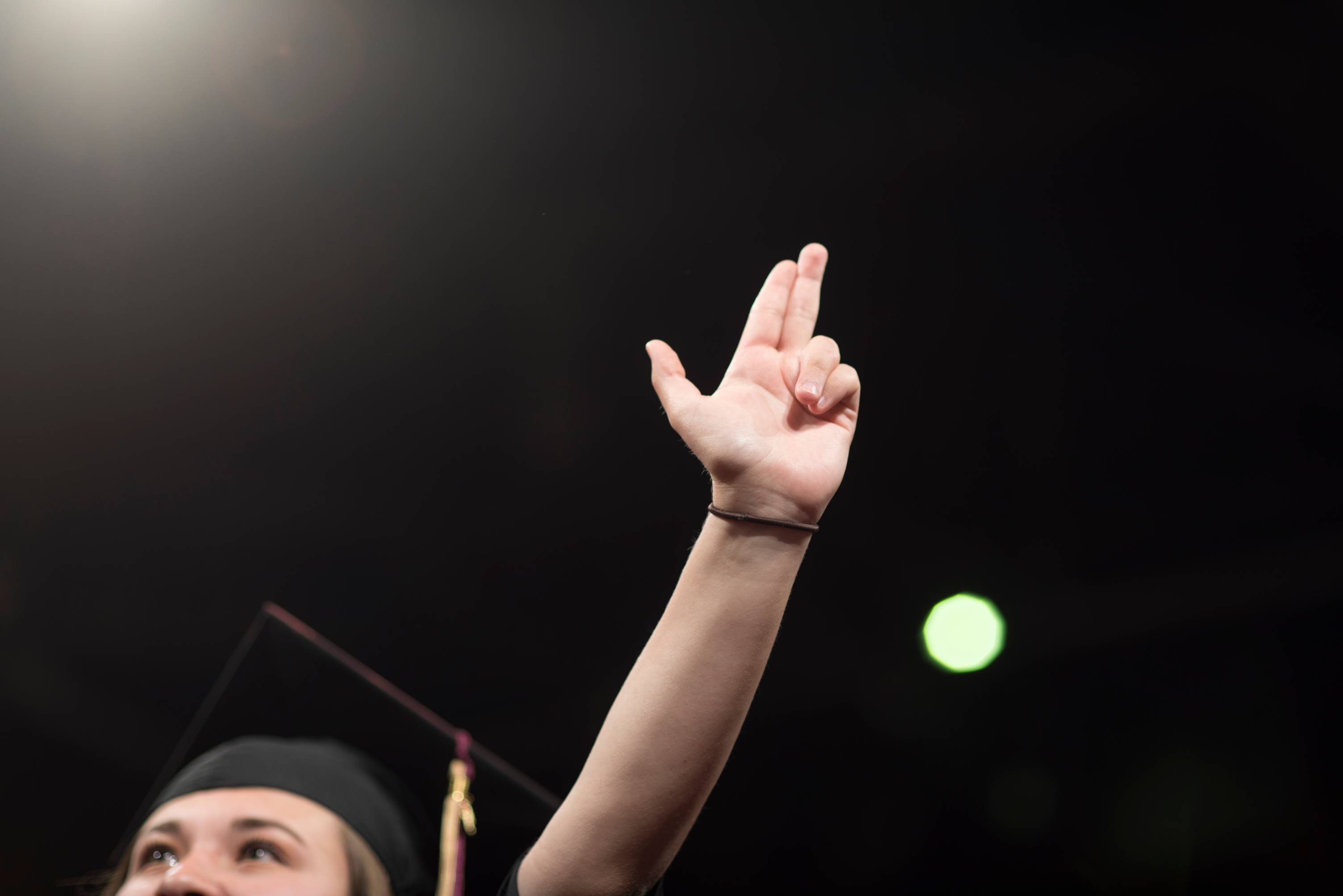 Picture of dark background with a student's hand in the air forming the shape of Texas