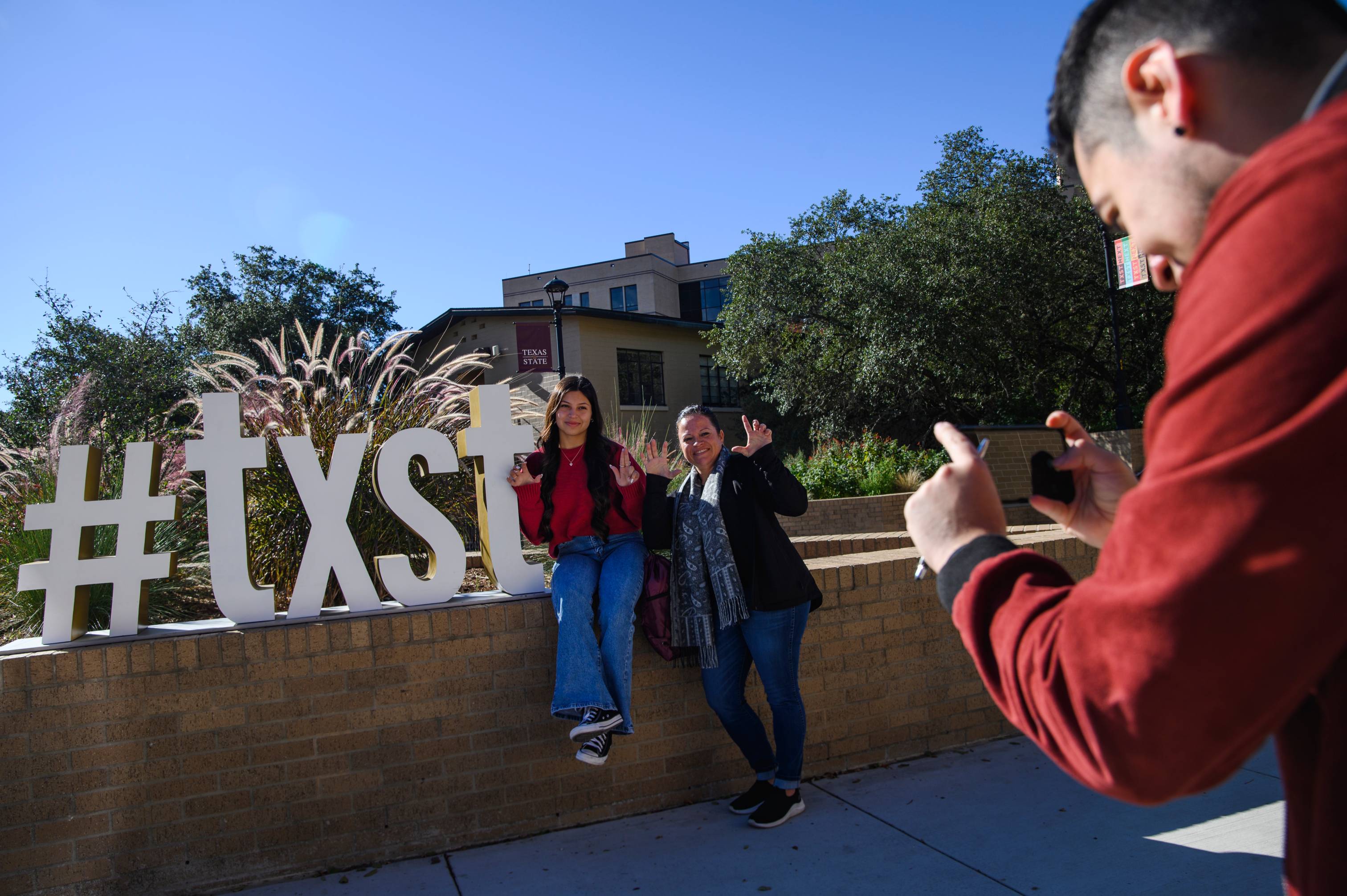 Student with their guardian sitting in front of the #txst sign getting their picture taken