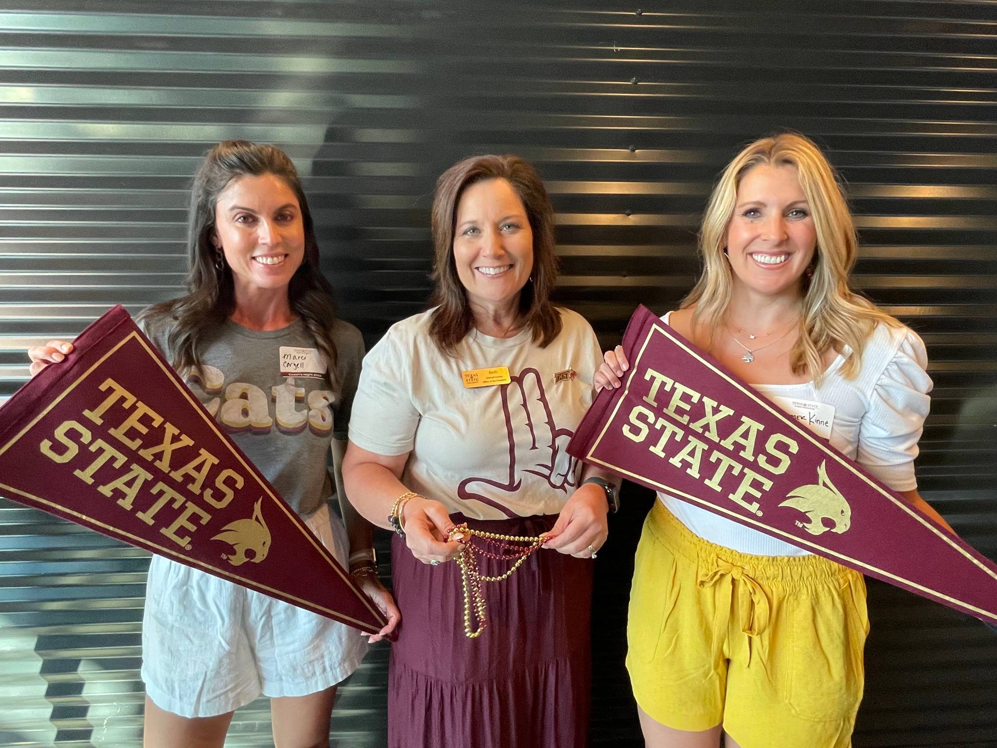 Group of three people holding TXST flags, wearing TXST merch