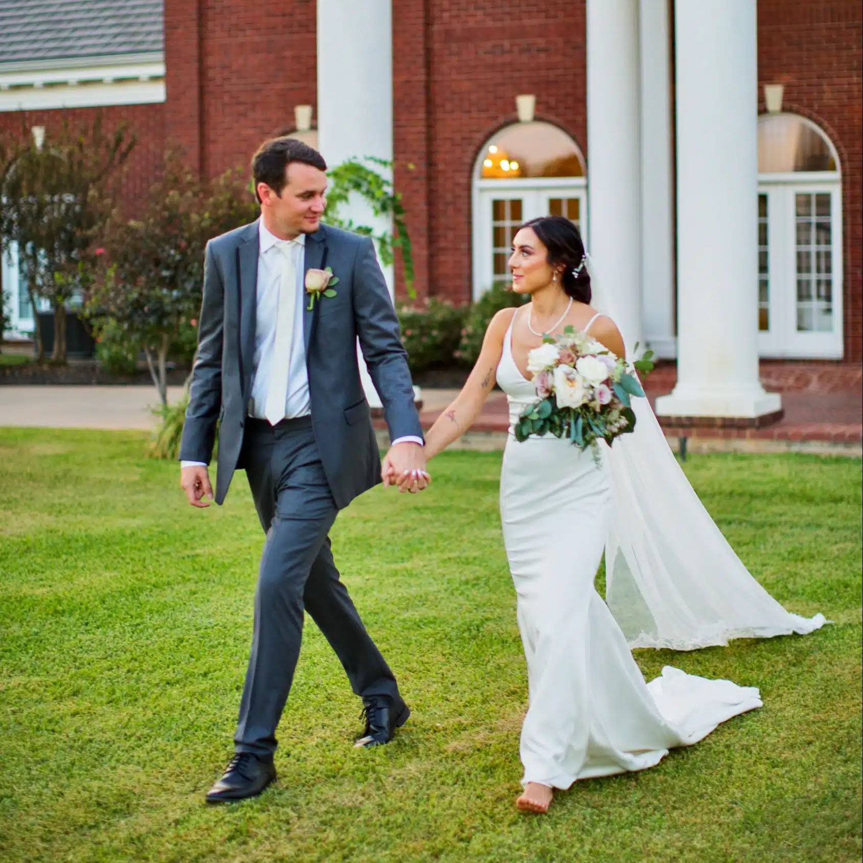 Photo of couple in wedding attire walking in grass