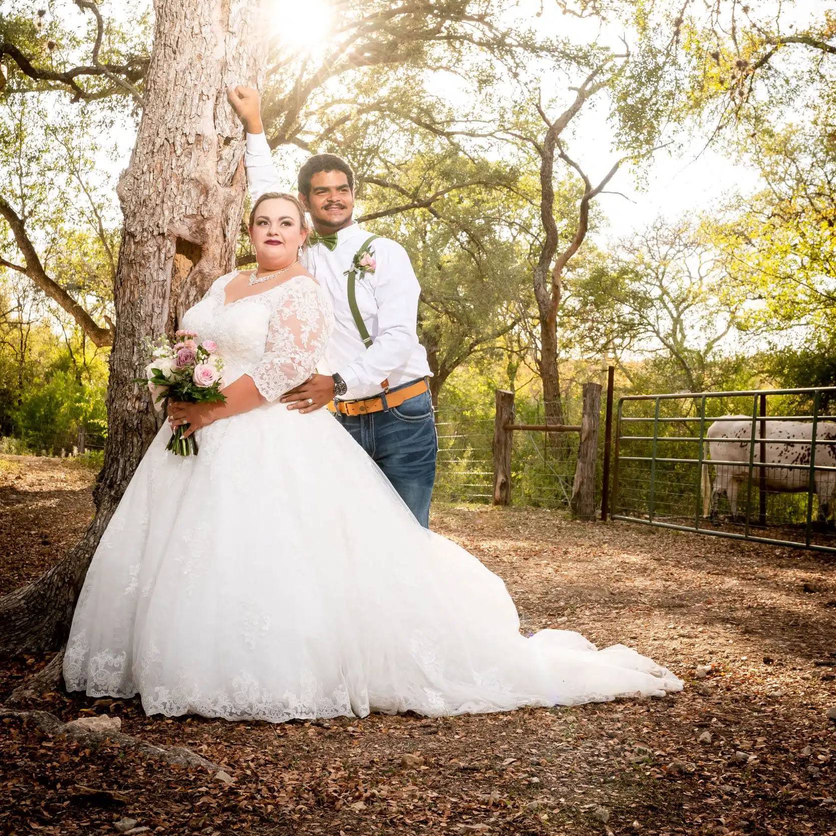 photo of couple in wedding attire standing by a tree