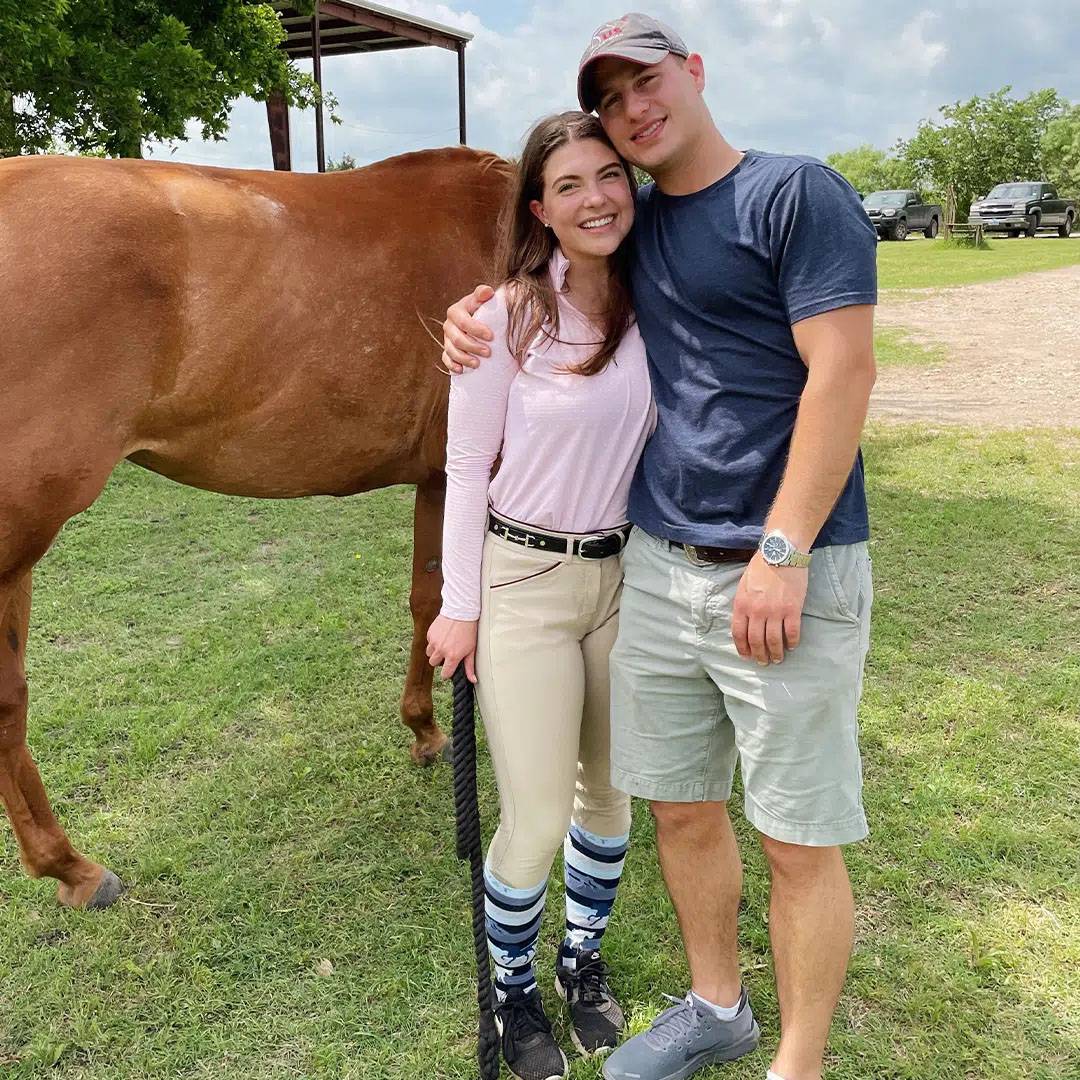 photo of couple standing together smiling in front of a horse