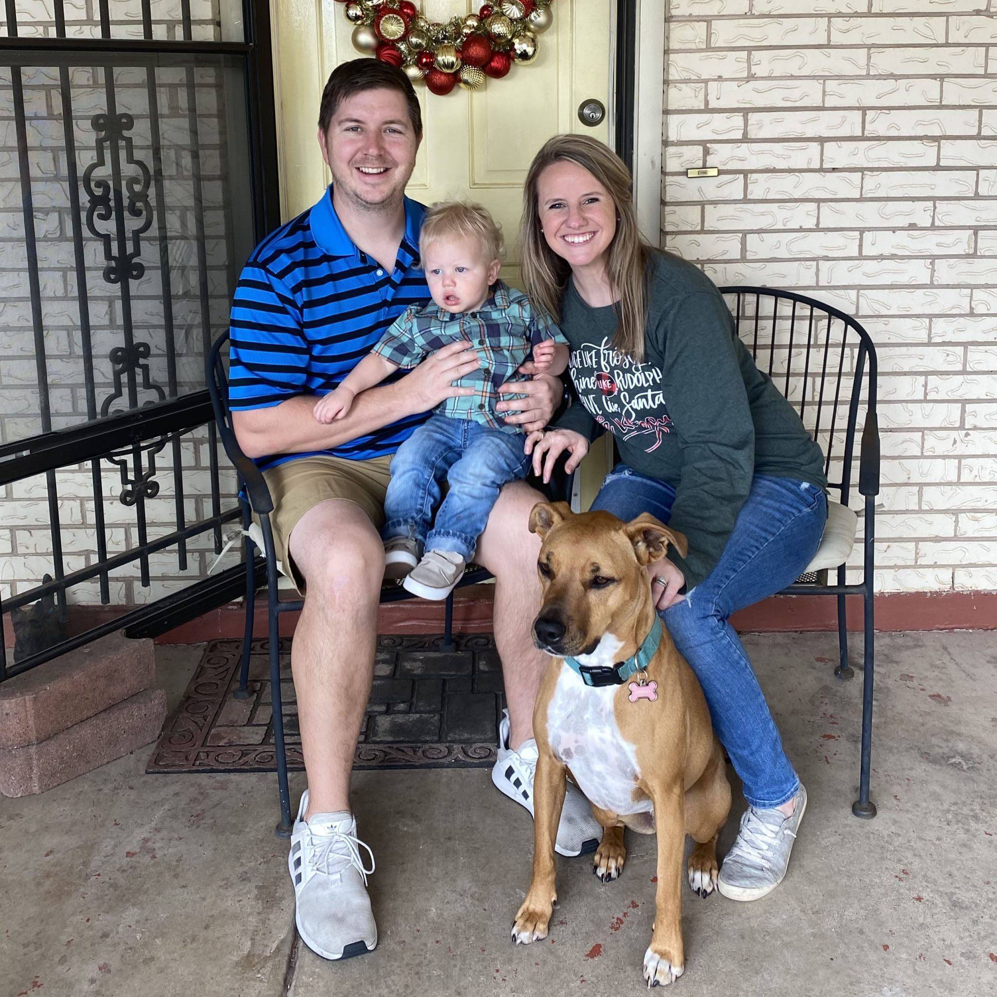 Photo of couple with baby and a dog, sitting on a bench and smiling