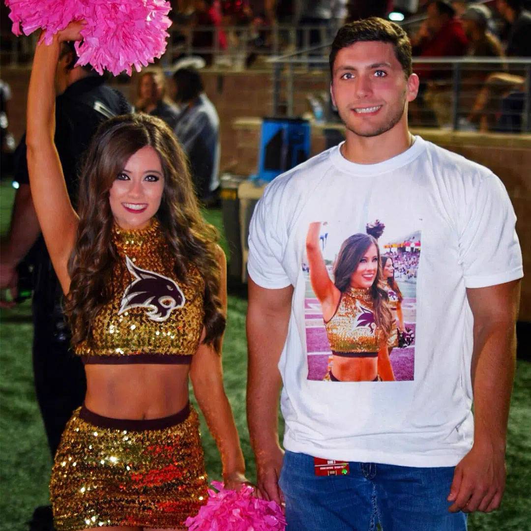 Photo of couple at football game, man is wearing shirt with woman in uniform, woman is wearing dance uniform