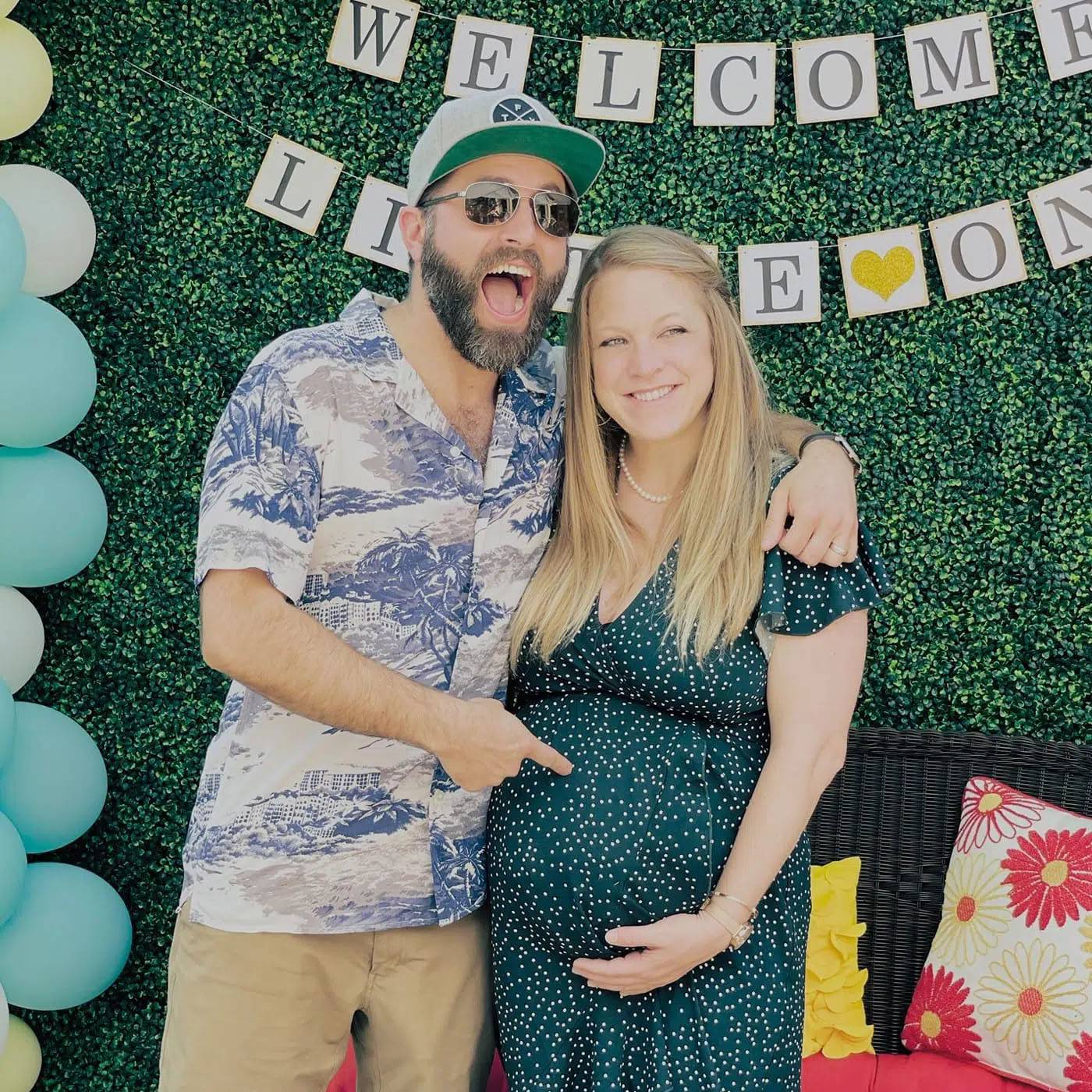 Photo of couple at baby shower, woman is pregnant, man is pointing to her belly