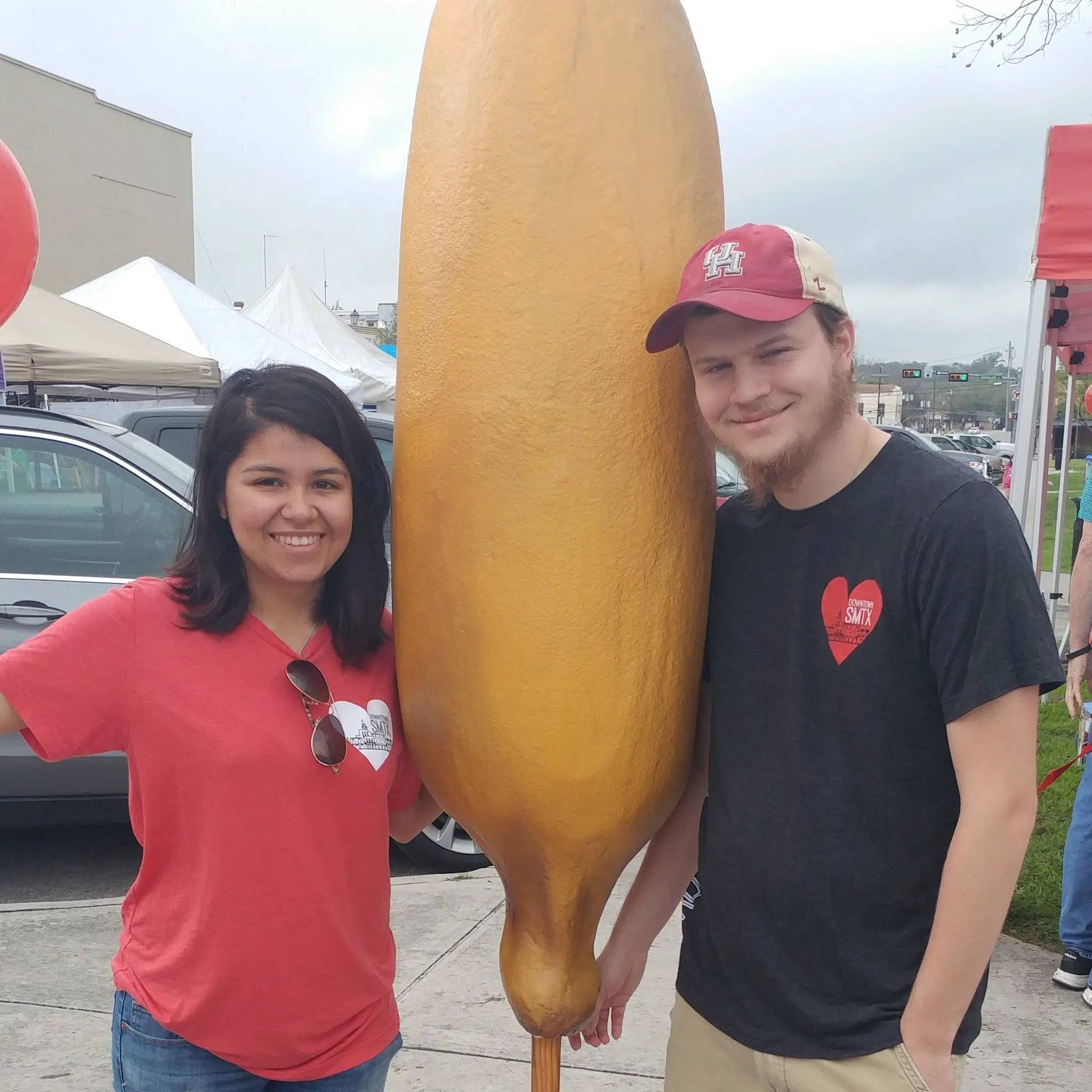 Photo of couple standing together next to a giant corndog