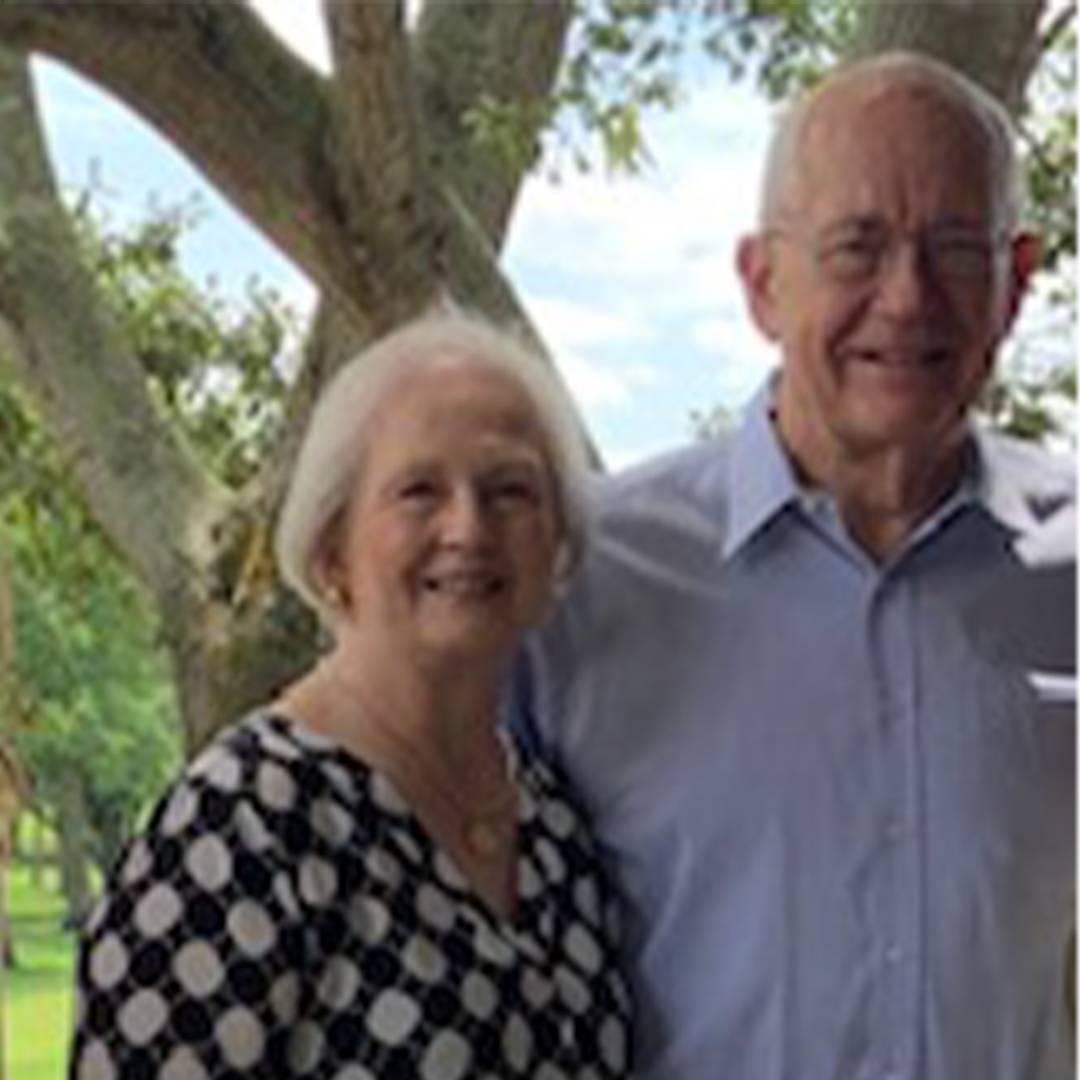 Photo of couple standing together smiling by a tree