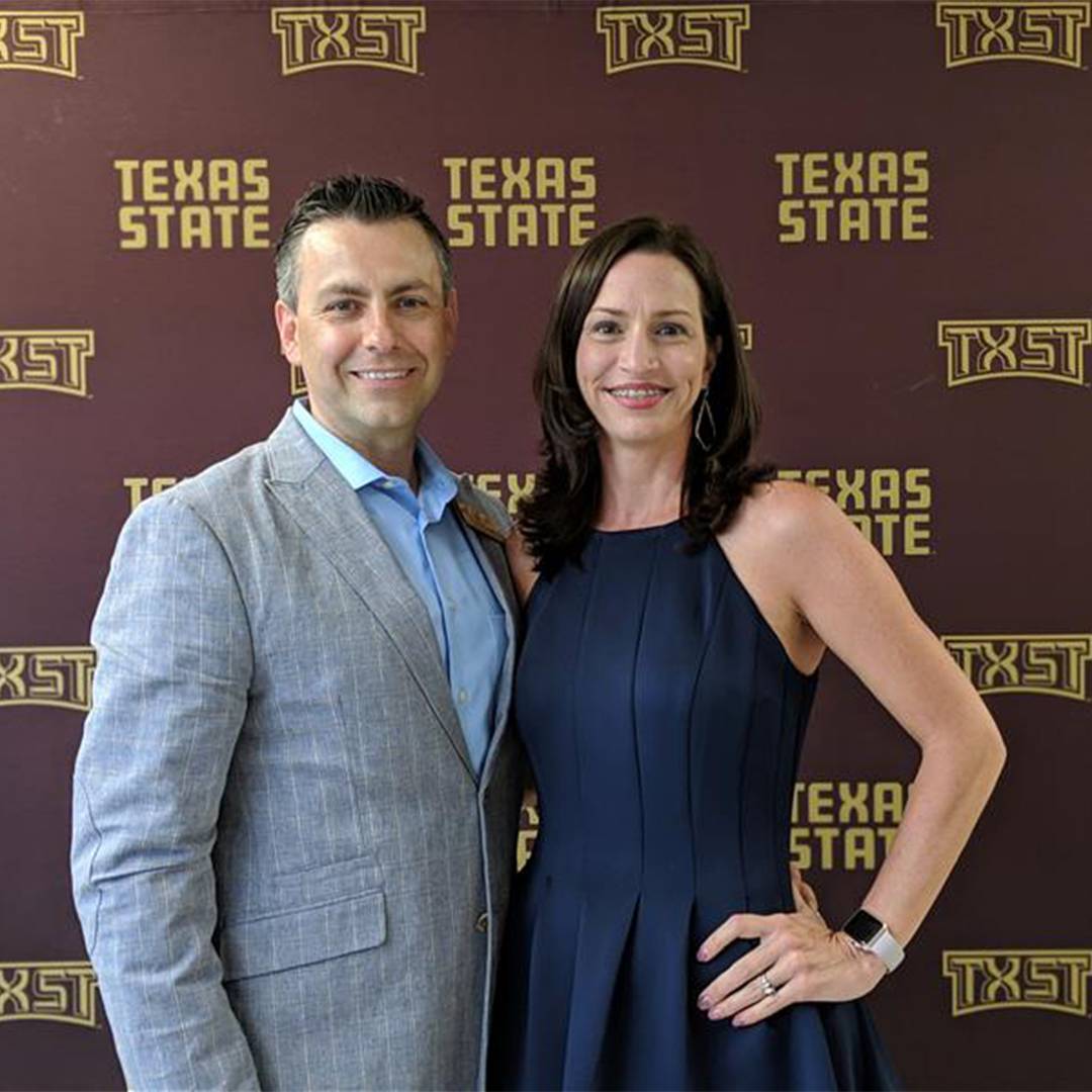 Photo of couple smiling against TXST branded background