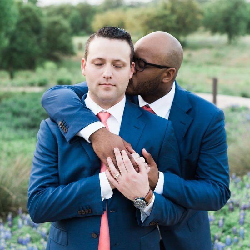 Photo of couple holding each other in a field wearing matching blue suits