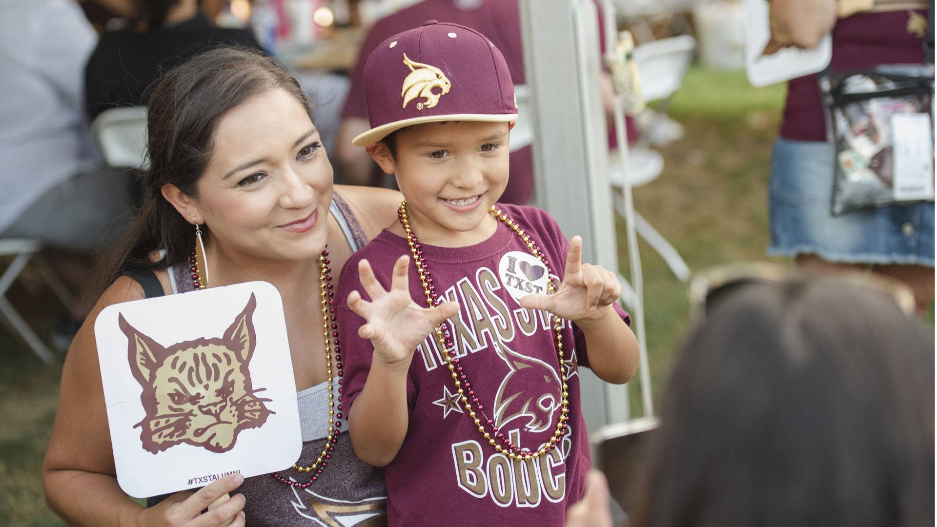 Woman holding Texas state alumni sign next to her child wearing bobcat merch.