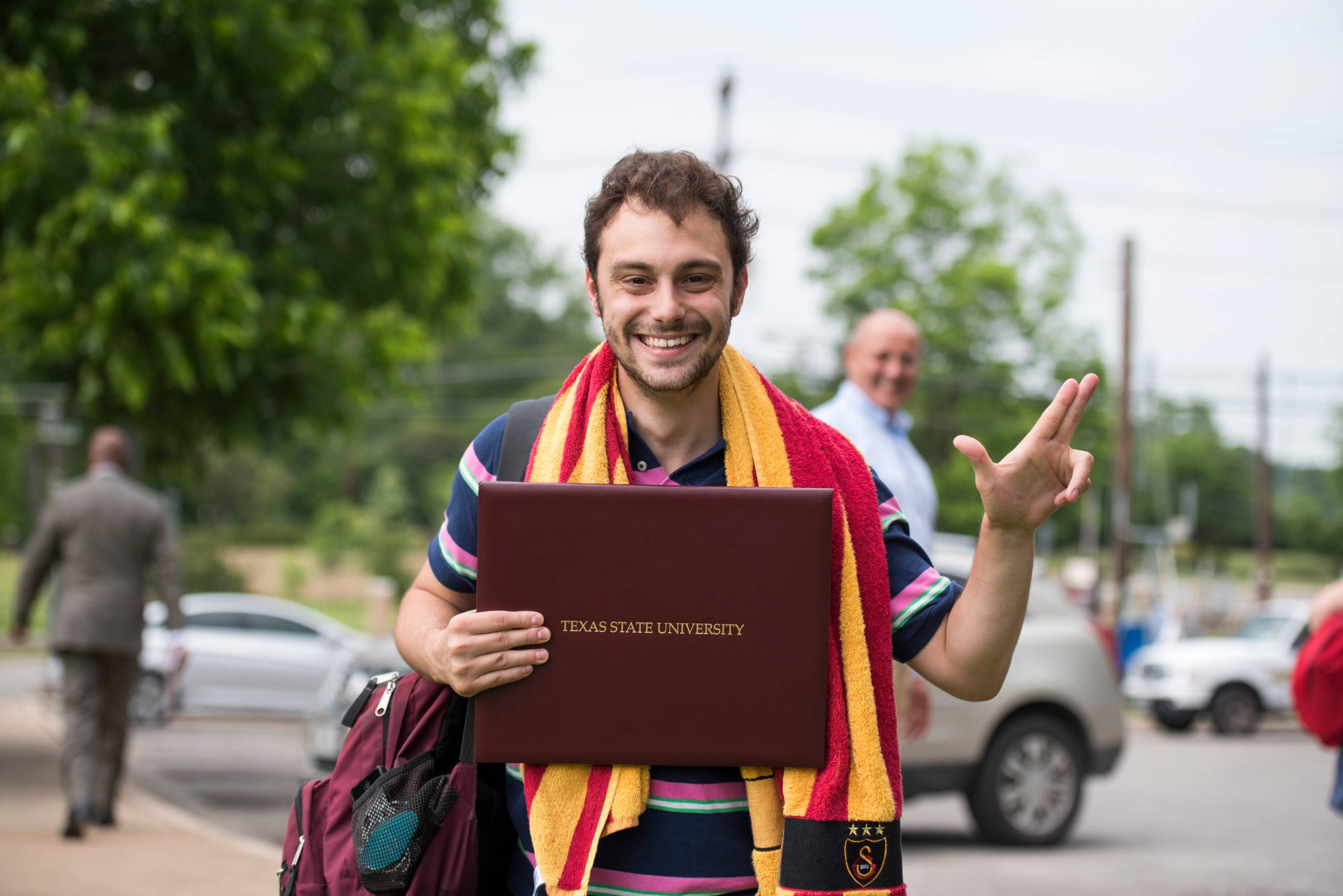 graduating student with TXST hand sign