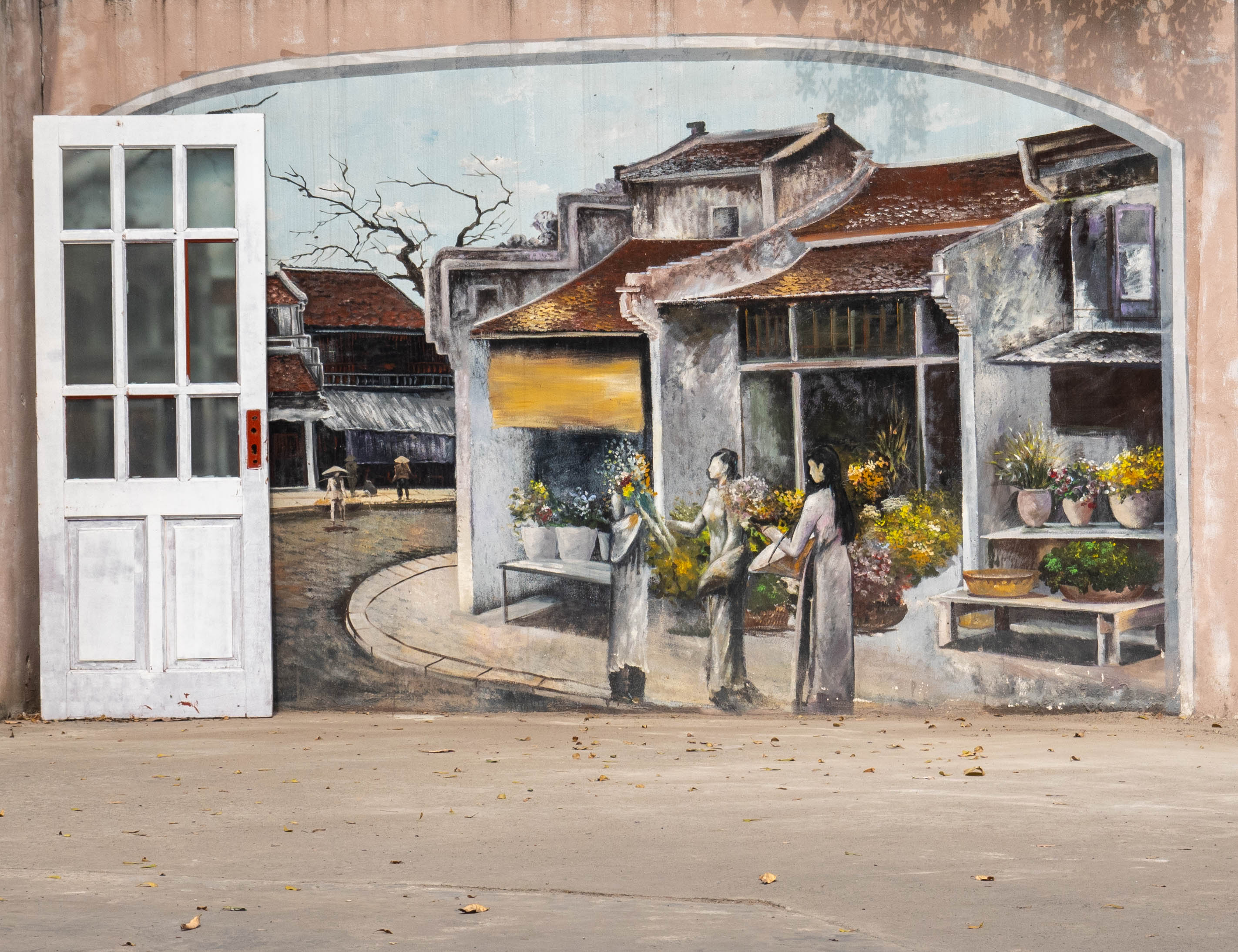 mural on wall showing a street corner with two ladies dressed in traditional Áo dài. On the left side of picture there is a door leaning against the wall.
