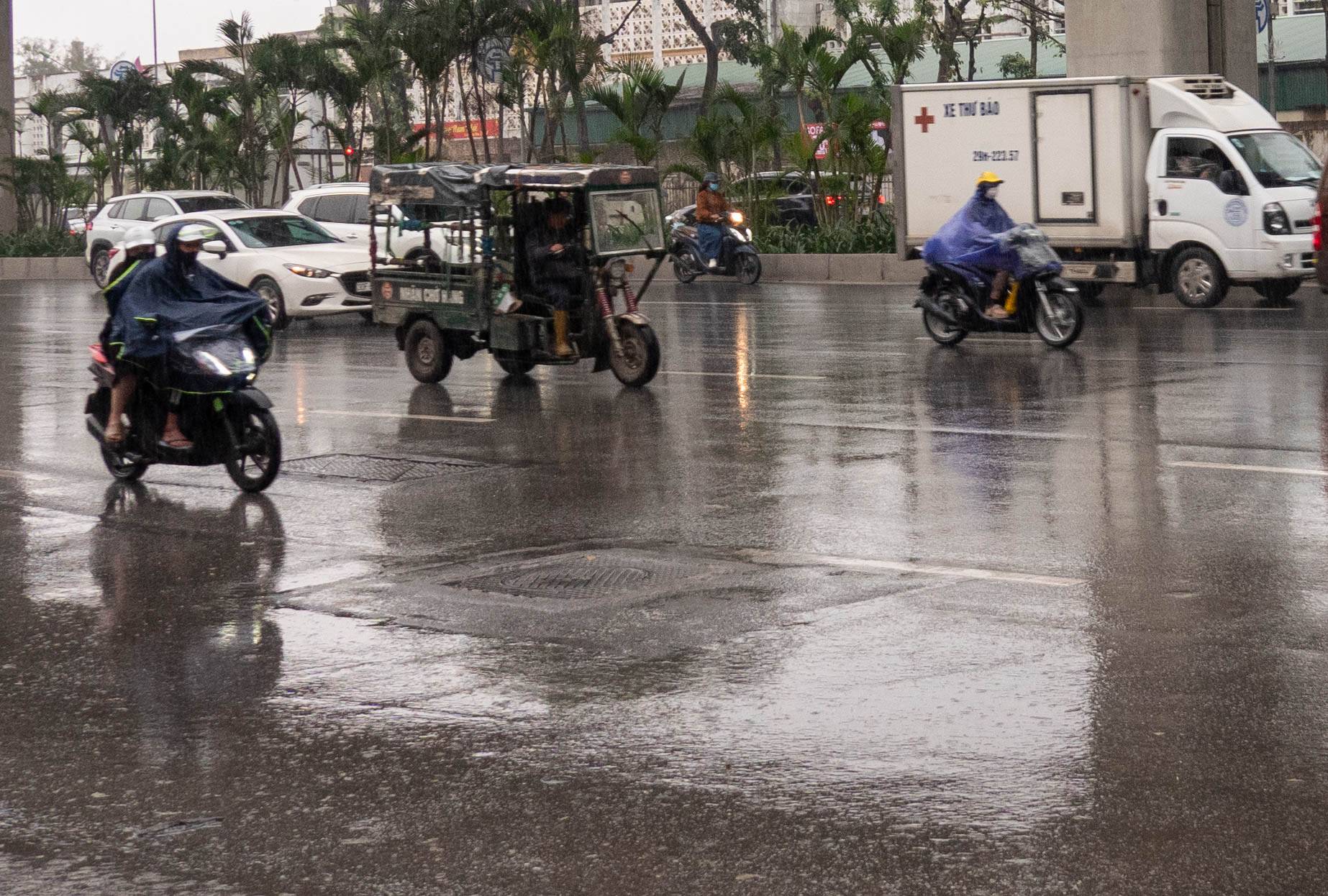 Picture of motorbikes, cars, and a three wheel vehicle on a rainy day
