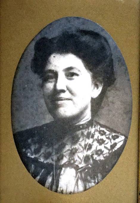 Aged black and white photo of Elena Zamora O'Shea. She appears to be in her 20s, and has light skin and dark, wavy hair styled into an up-do. She's wearing a high-necked dress with a floral lace collar. 