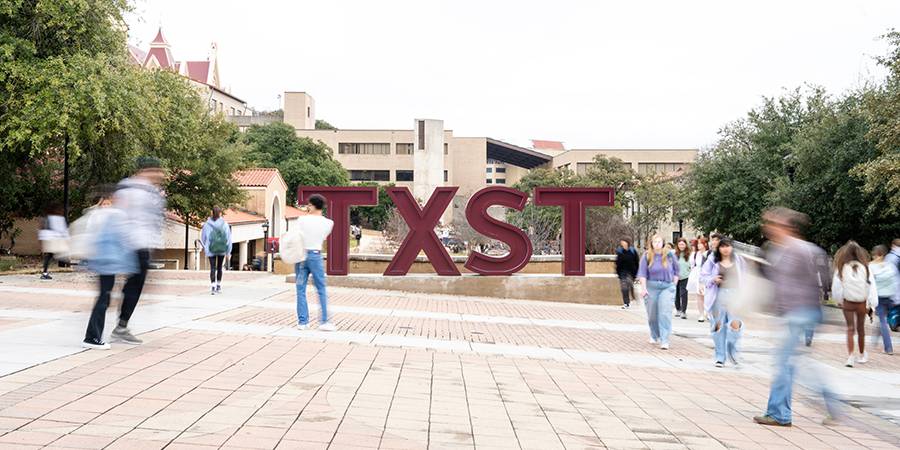People walking in front of the TXST sign on campus