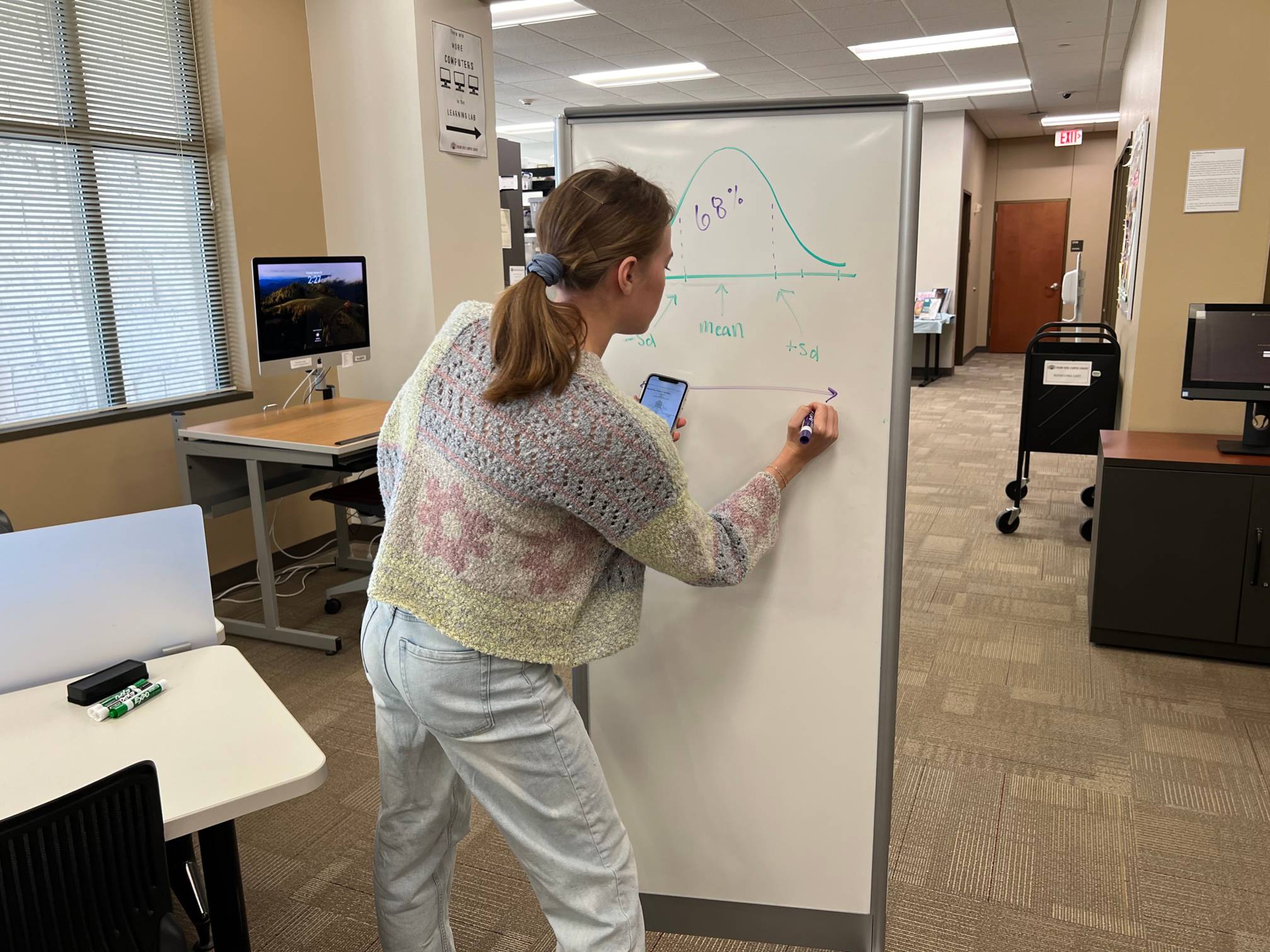 An individual writing on a dry erase board referencing a smartphone.