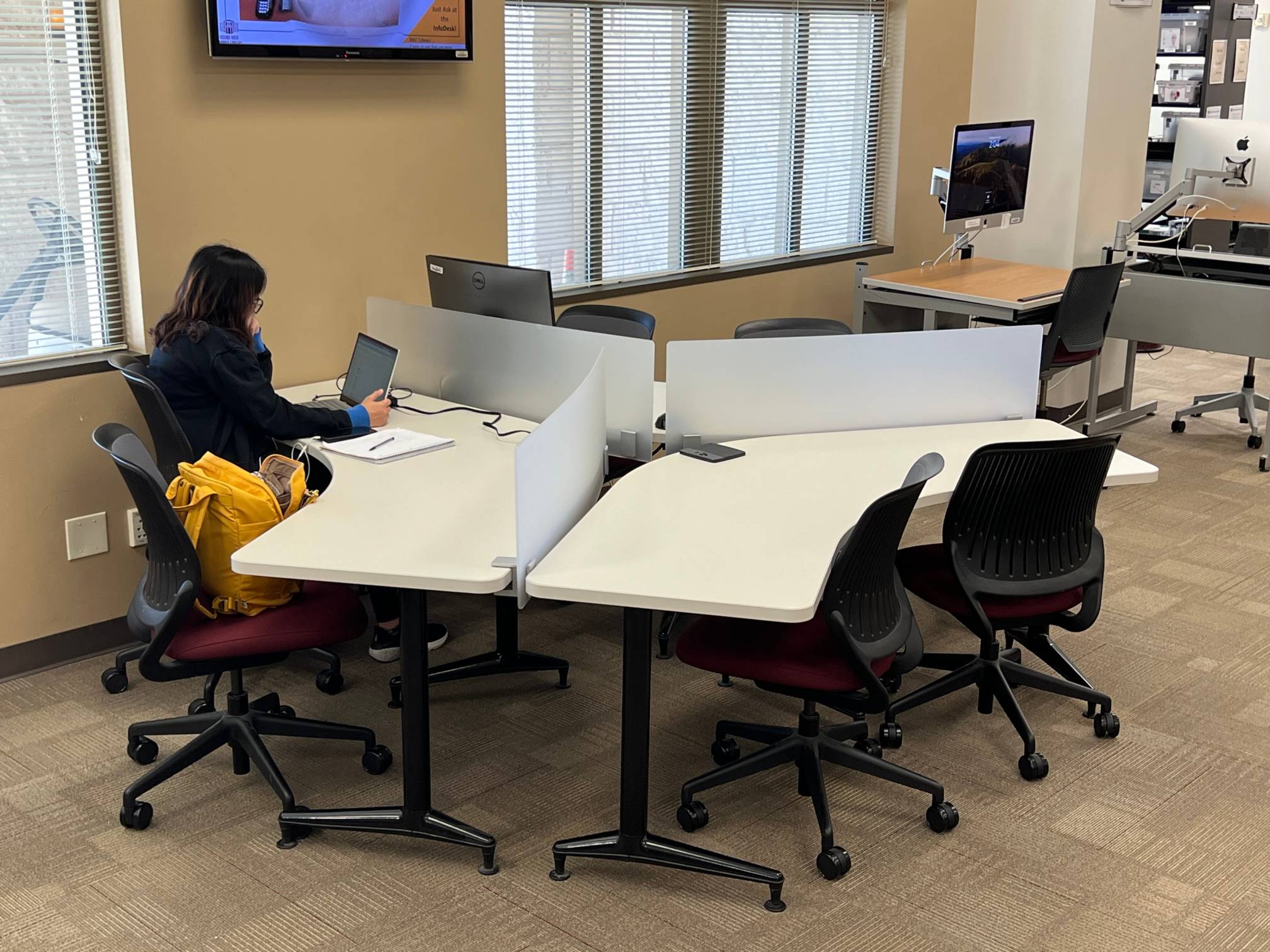 a person using a laptop sitting at a Y-shaped table containing six chairs and a computer