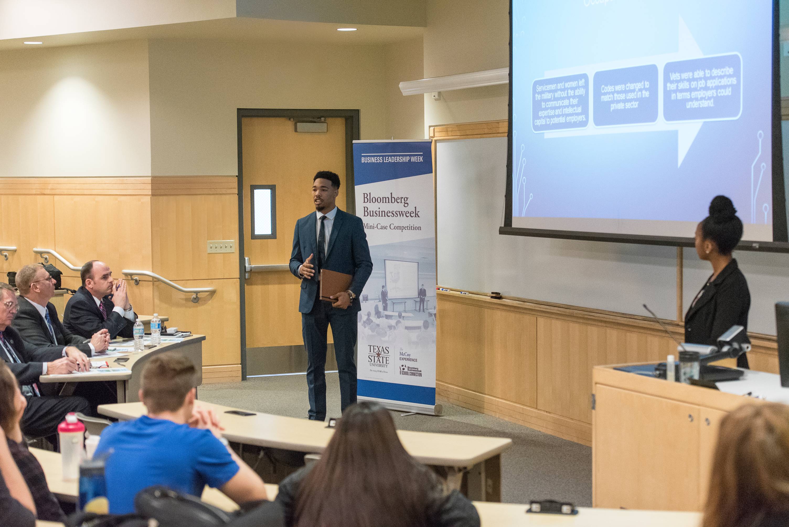 two students in front of a classroom room giving a presentation