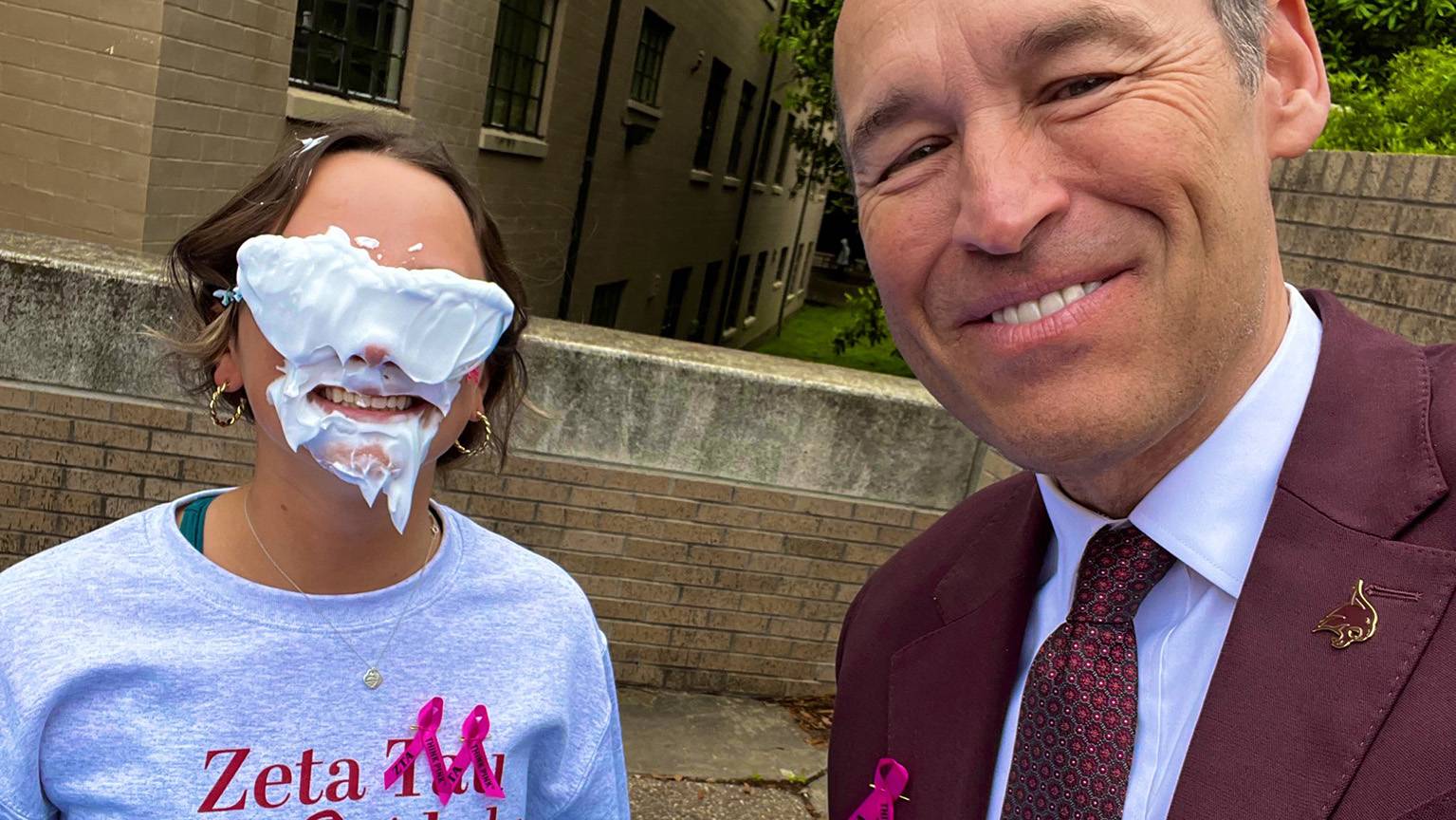 President Damphousse, right, poses for a photo with a student with pie covering her face.